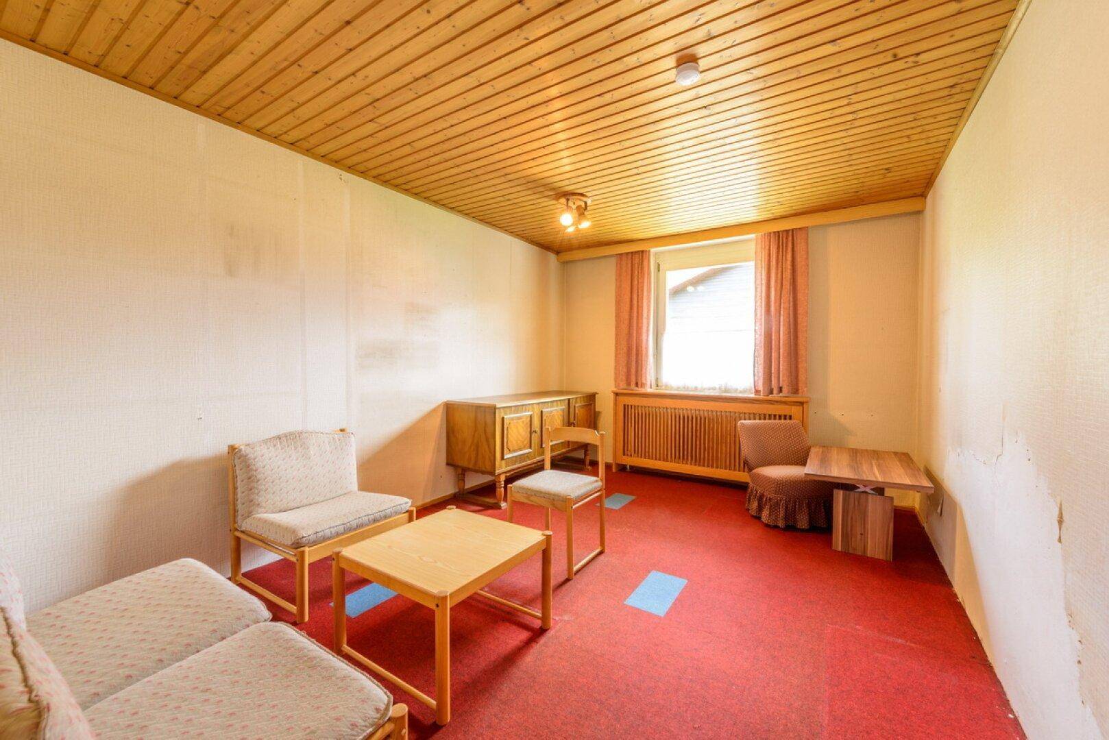 Einfaches Wohnzimmer mit rotem Teppichboden, Holzmöbeln und Fenster.