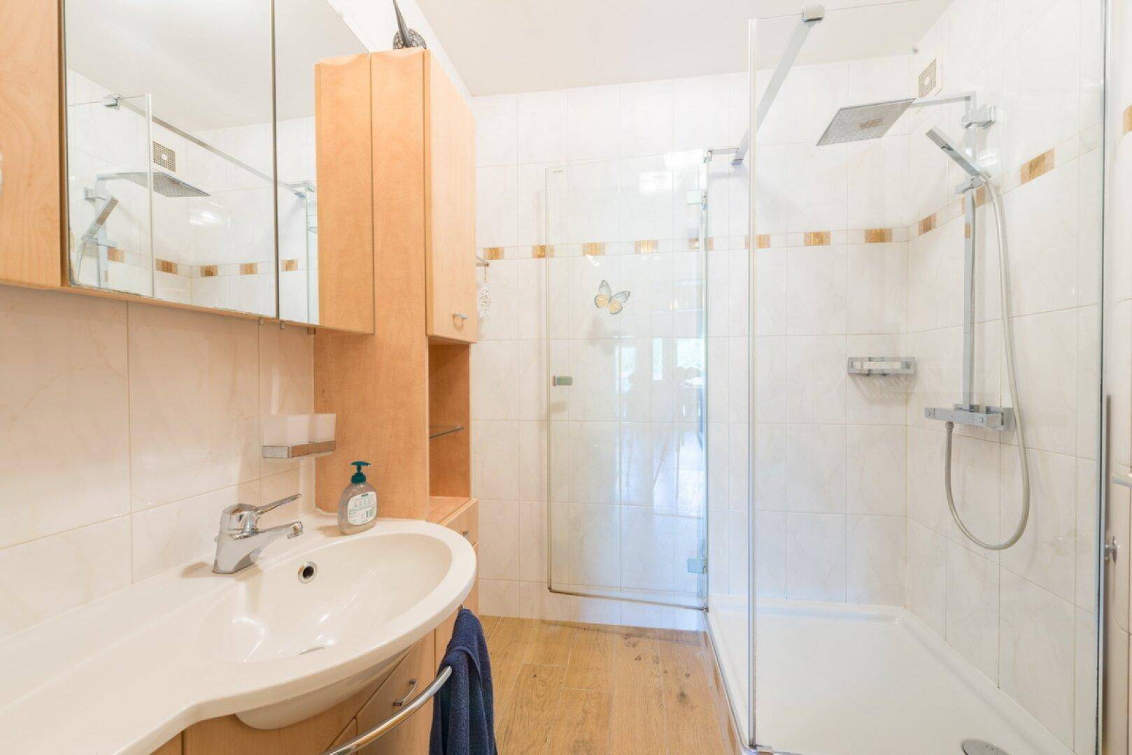 Modernes Badezimmer mit Duschkabine, Waschbecken, Spiegelschrank und hellen Fliesen.