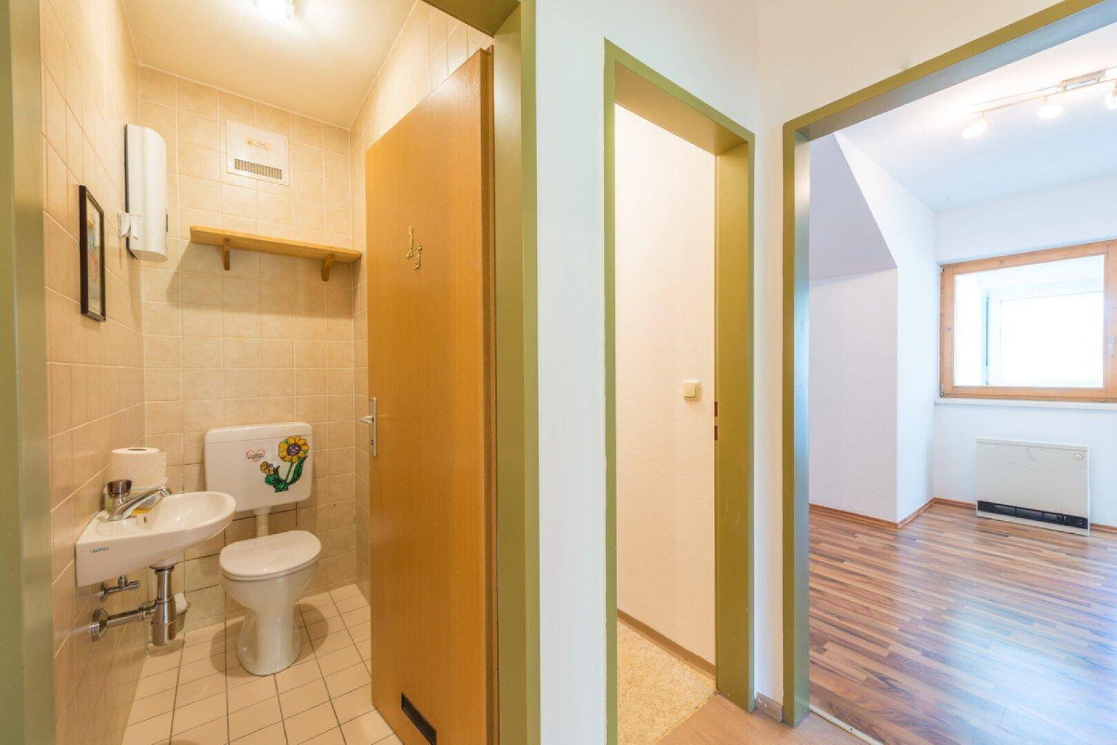 Kleines Gäste-WC mit beigefliesten Wänden, Waschbecken und WC mit Blumenmuster.