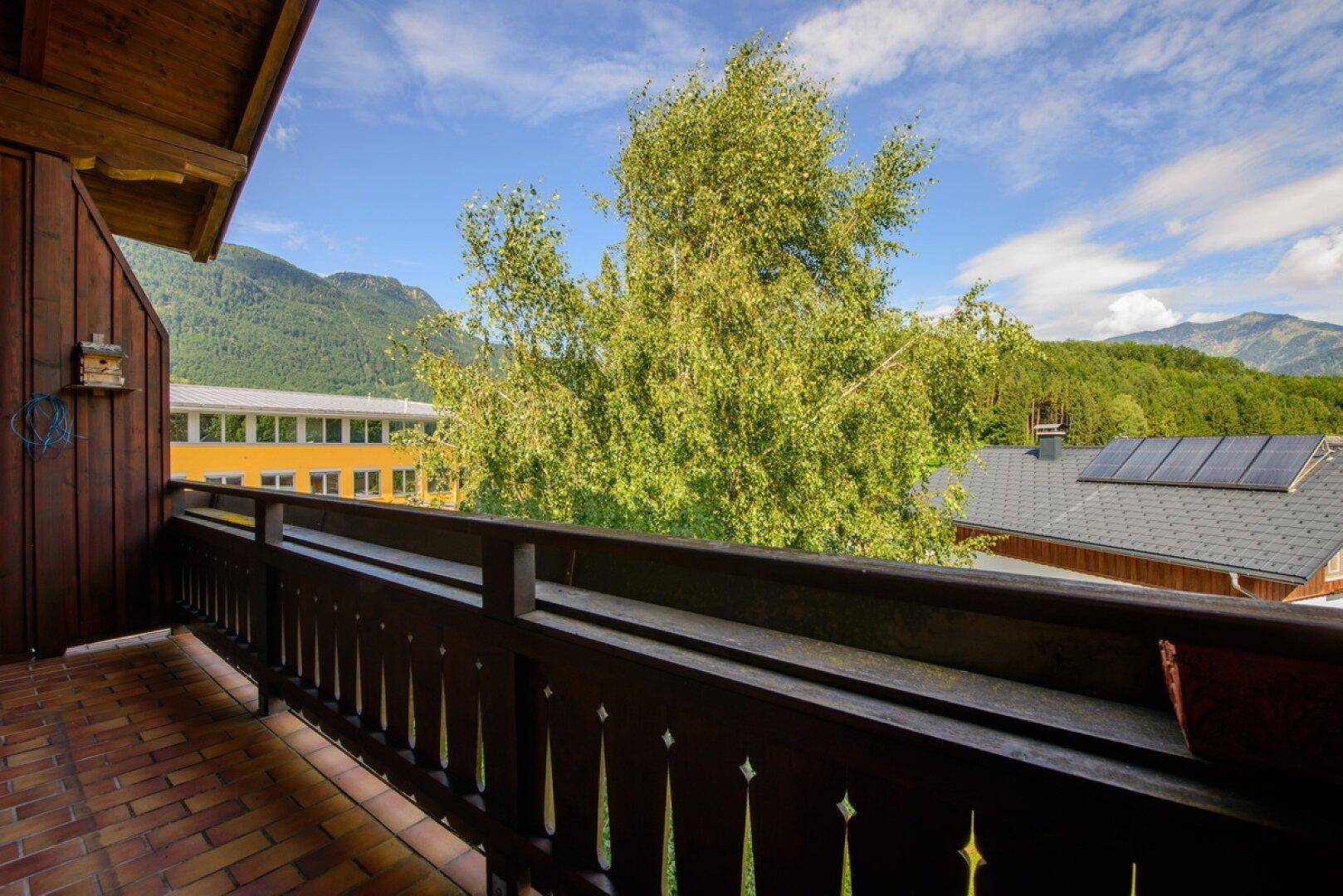 Balkon mit Holzboden und Geländer, bietet einen weiten Blick auf die umliegenden Berge und Bäume.