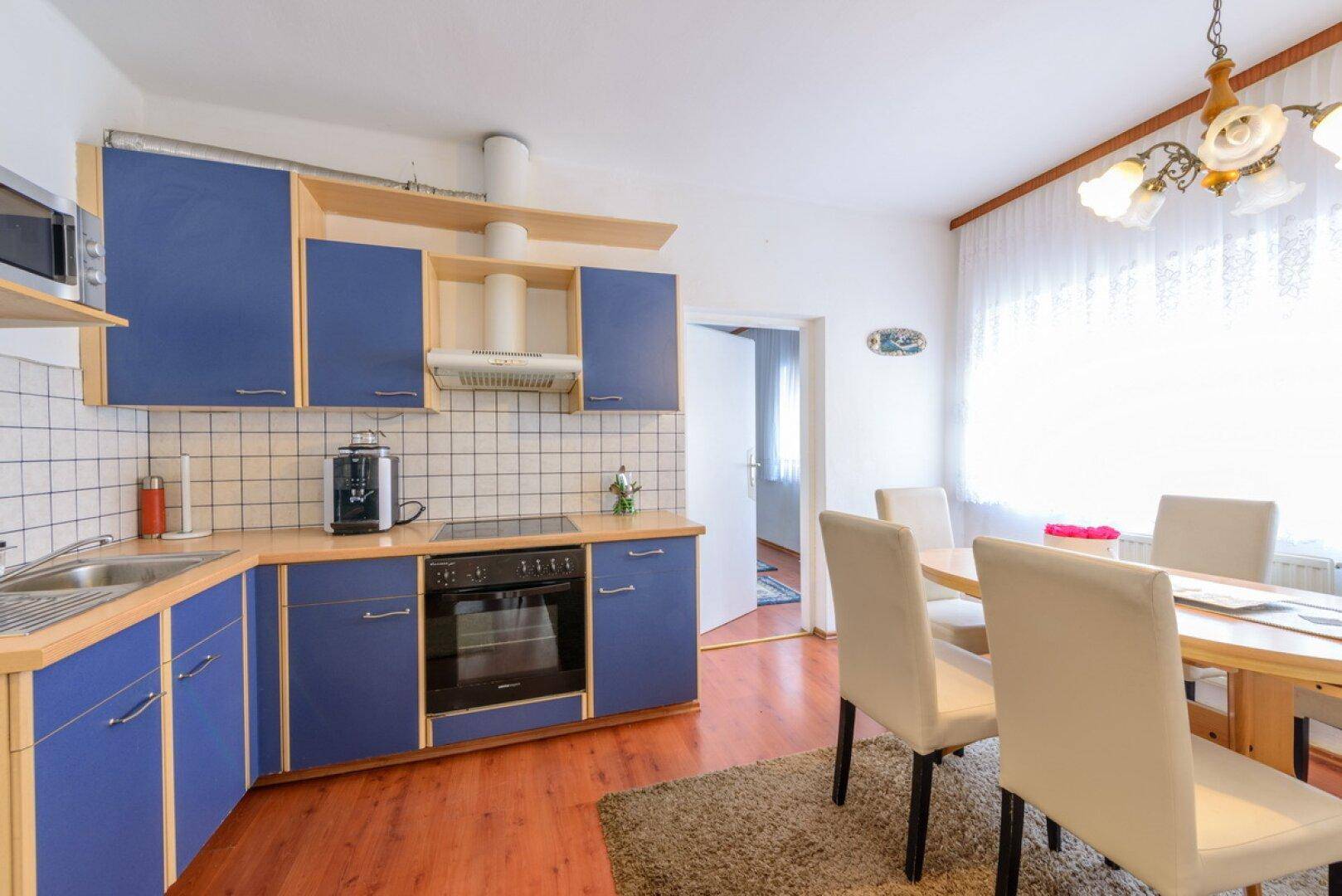 Küche mit blauen Unterschränken, Holzarbeitsplatte und einem Essbereich mit hellem Holztisch.