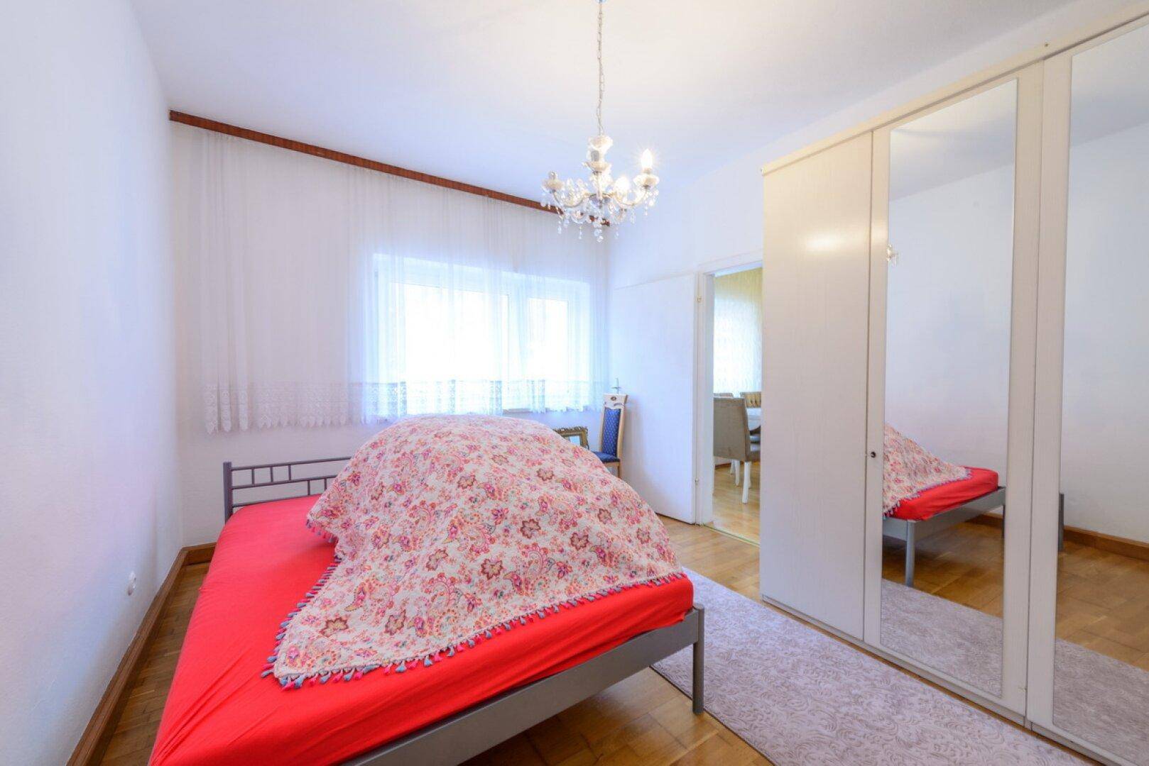 Schlafzimmer mit Doppelbett, Spiegelschrank und Holzboden, durchflutet von natürlichem Licht.
