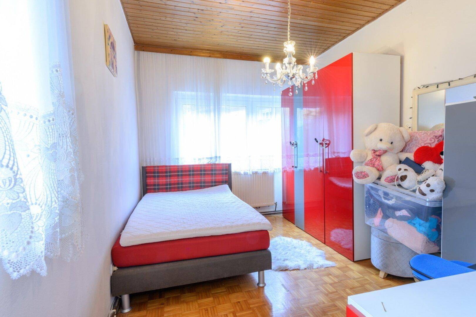 Kinderzimmer mit Einzelbett, farbenfrohem Kleiderschrank und Holzdecke, hell und freundlich gestaltet.