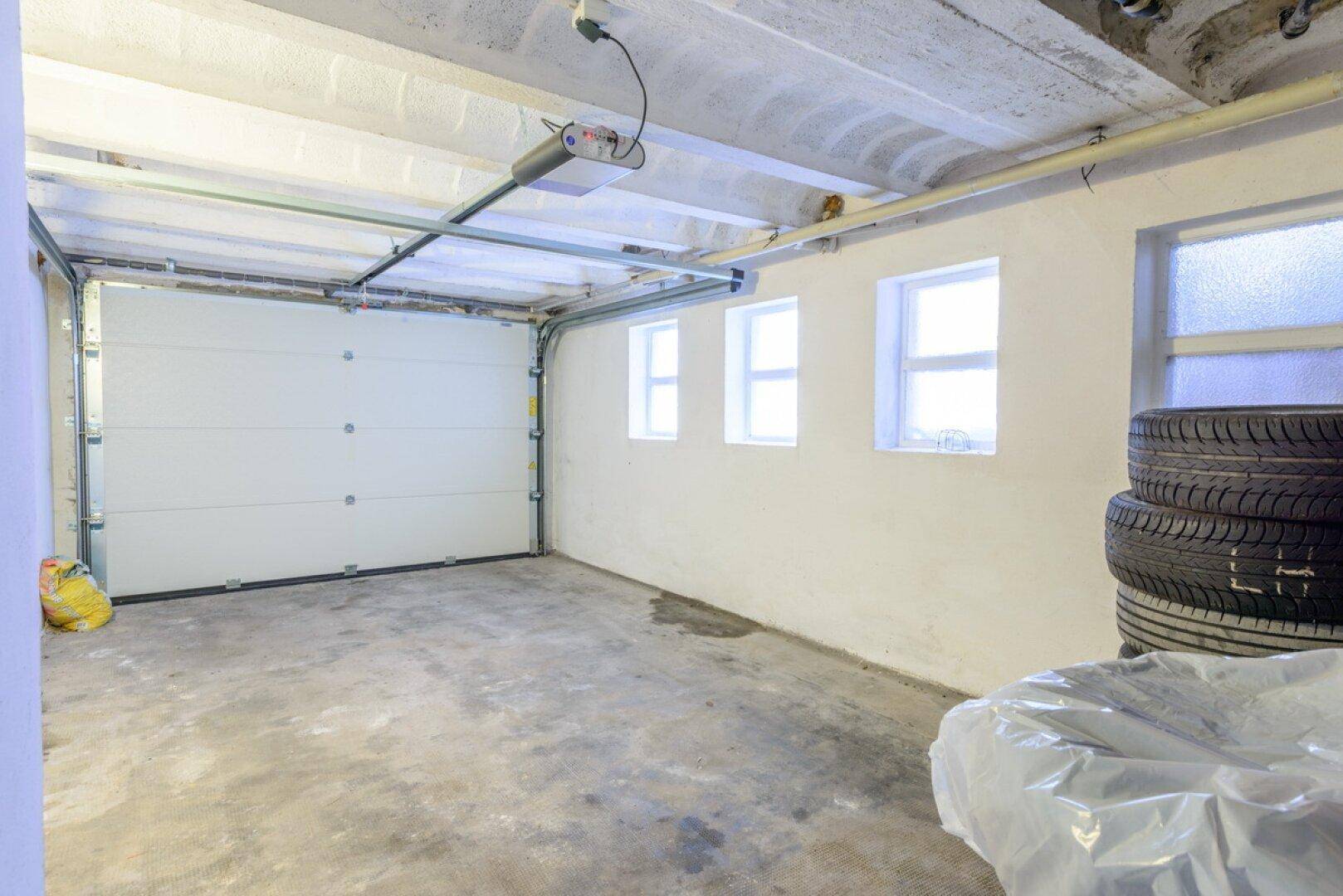 Geräumige Garage mit automatischem Tor, kleinen Fenstern und ausreichend Platz für ein Fahrzeug.