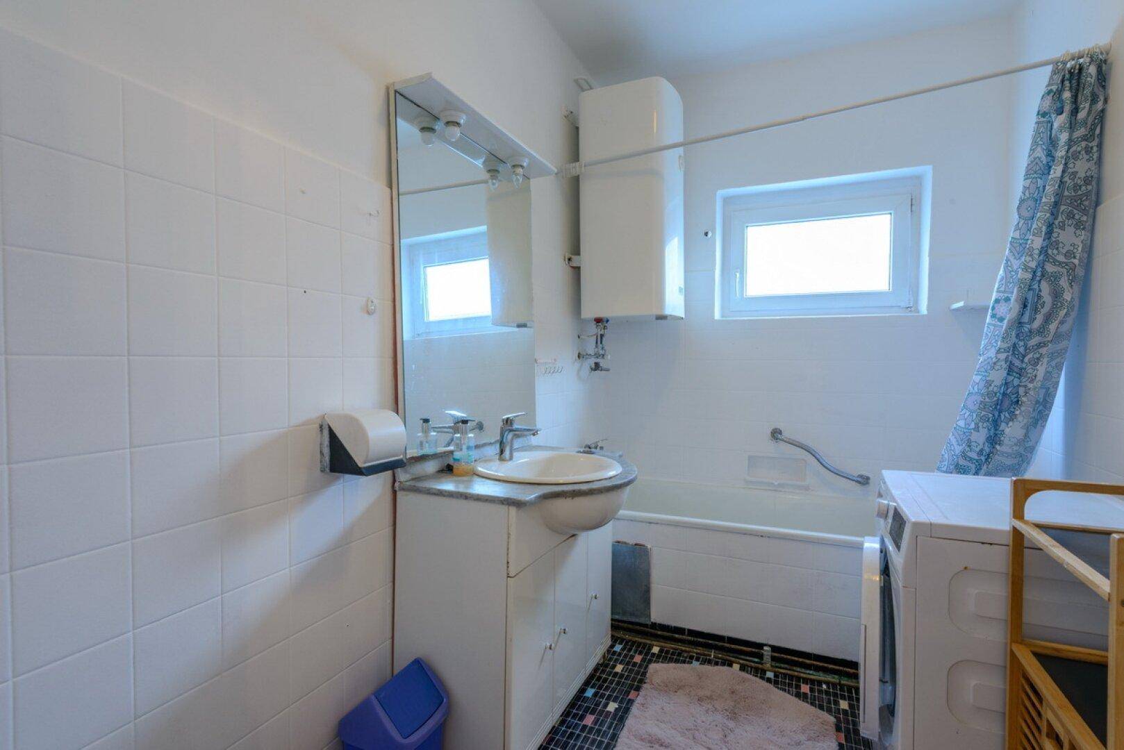 Badezimmer mit Badewanne, Waschbecken und weißen Fliesen, das Tageslicht durch ein Fenster erhält.