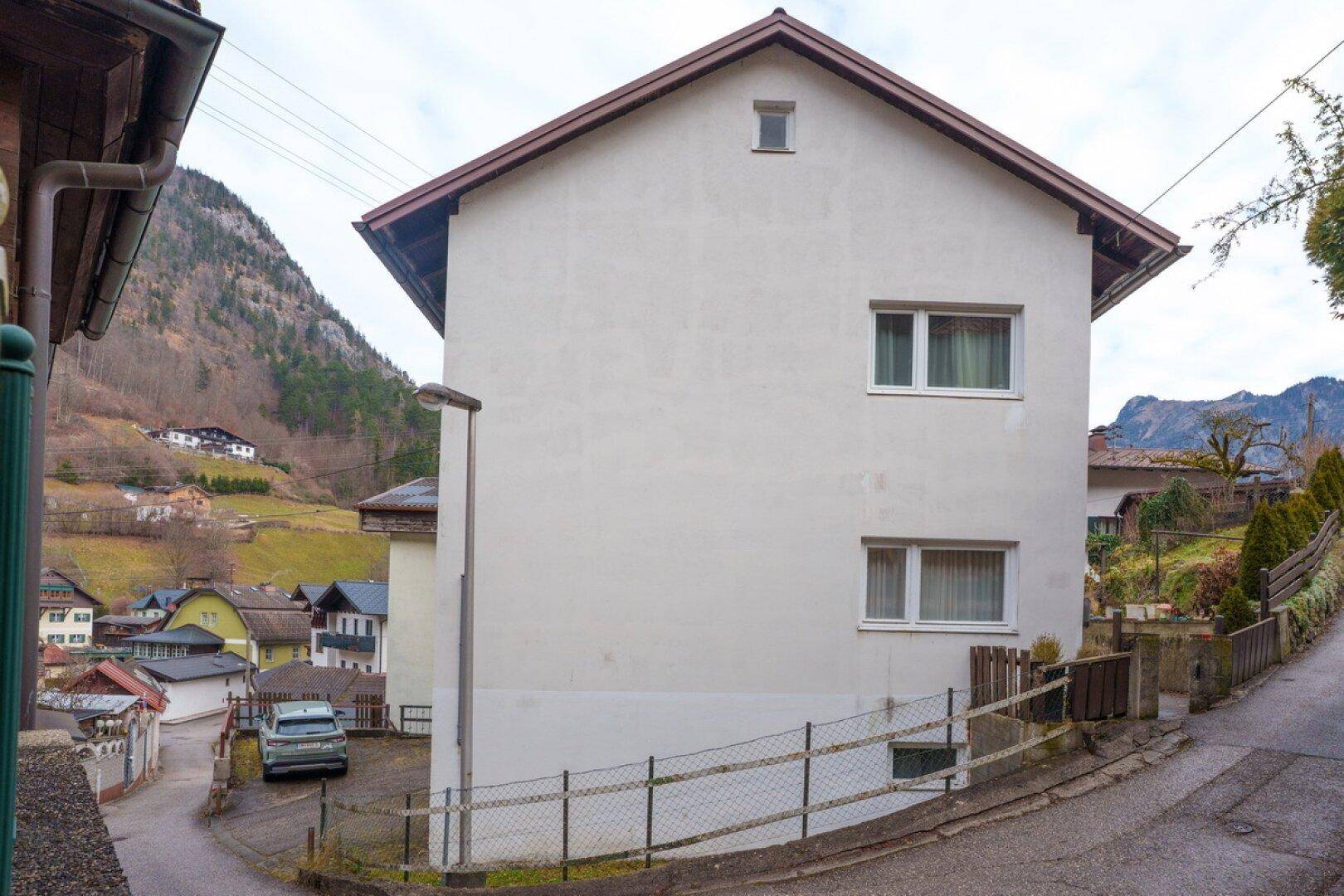 Seitenansicht des Wohnhauses mit weißer Fassade und Satteldach, umgeben von einer ländlichen Umgebung.