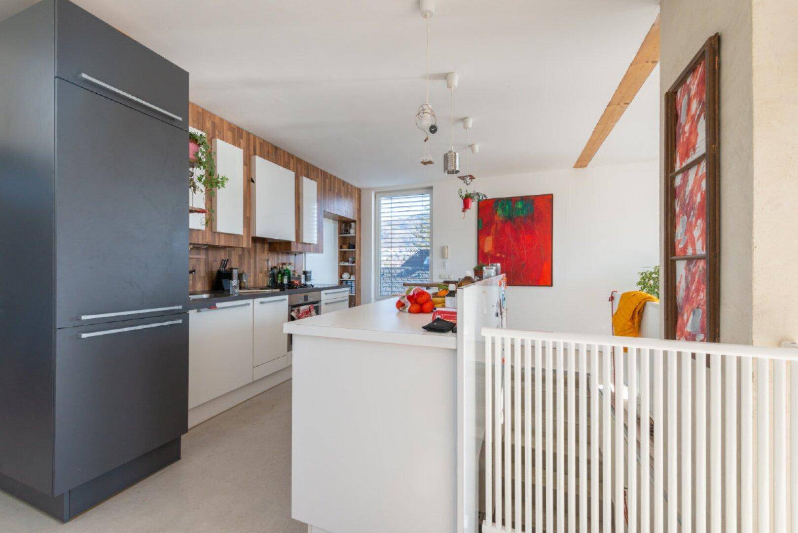 Moderne Küche mit weißer Kücheninsel, dunklem Kühlschrank und Holzvertäfelung an der Wand.