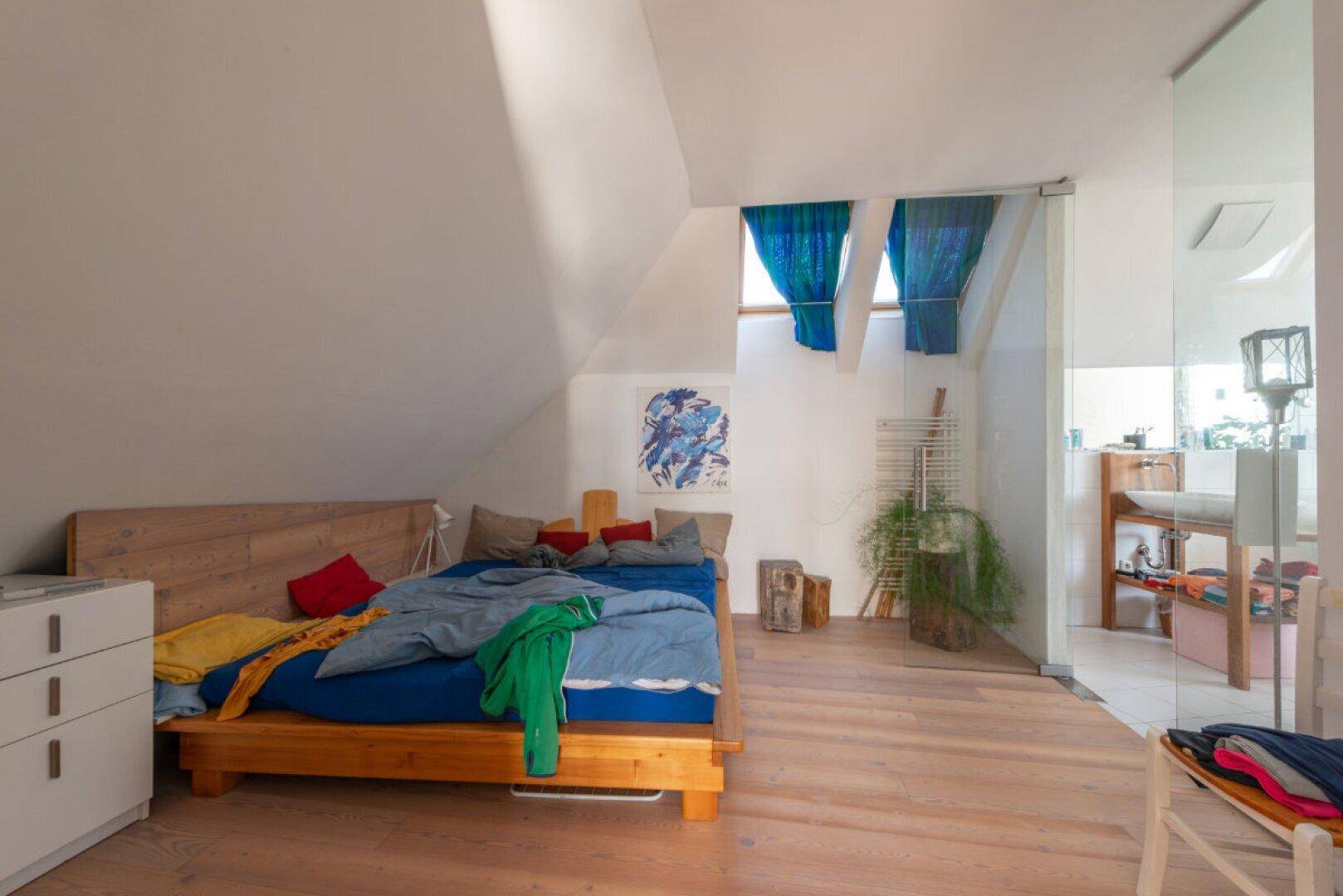 Helles Schlafzimmer im Dachgeschoss mit Holzbett, Holzboden und schrägen Wänden.