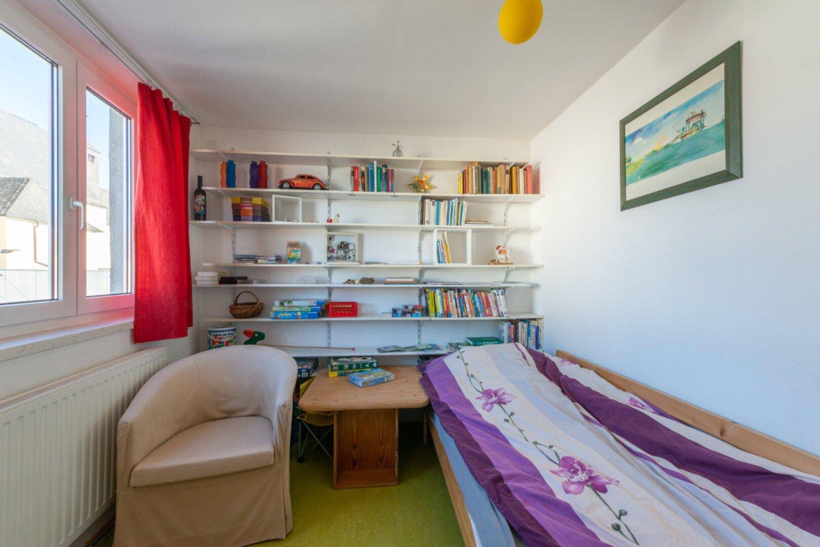 Kinderzimmer oder Gästezimmer mit Einzelbett, Bücherregal und grünem Teppichboden.