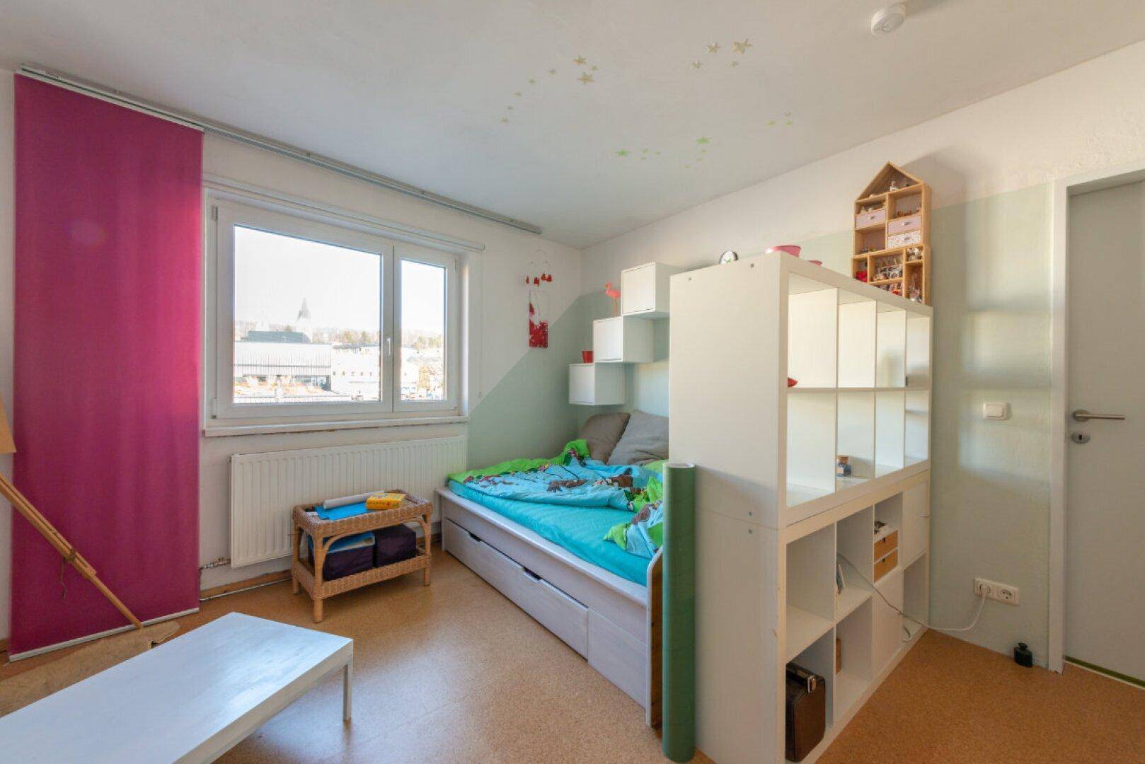 Helles Kinderzimmer mit Hochbett, Stauraum und Fenster mit Blick nach draußen.
