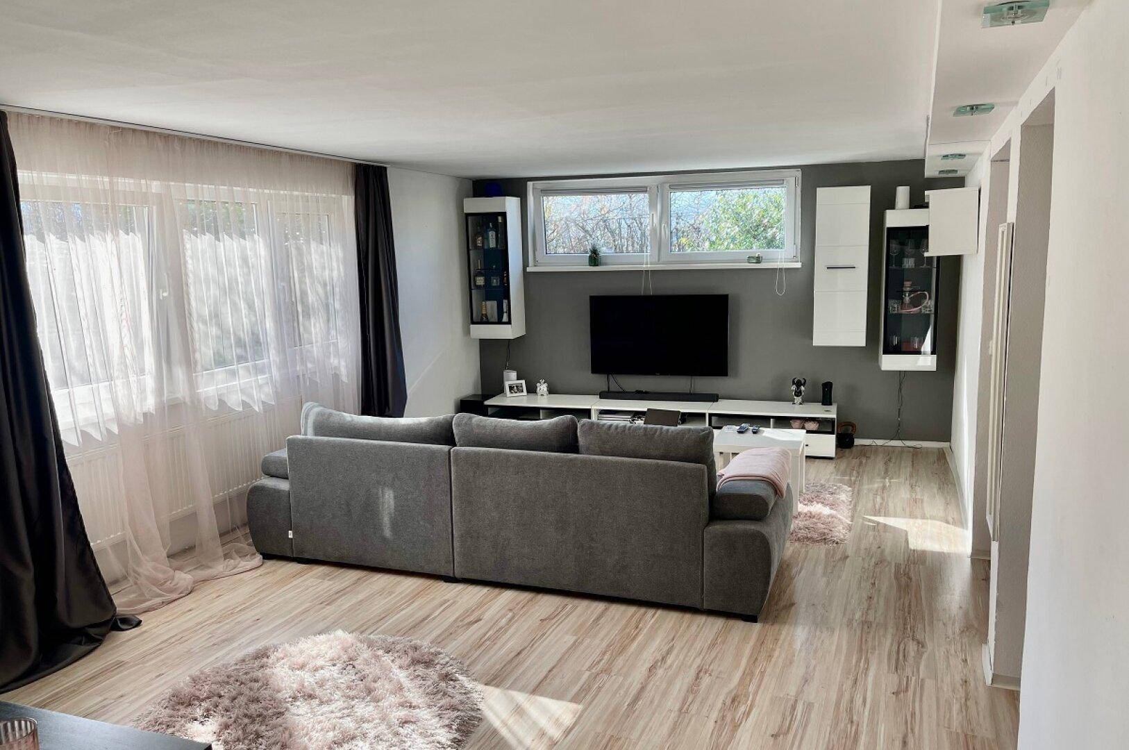 Gemütliches Wohnzimmer mit großem Sofa, Fernseher und Laminatboden.