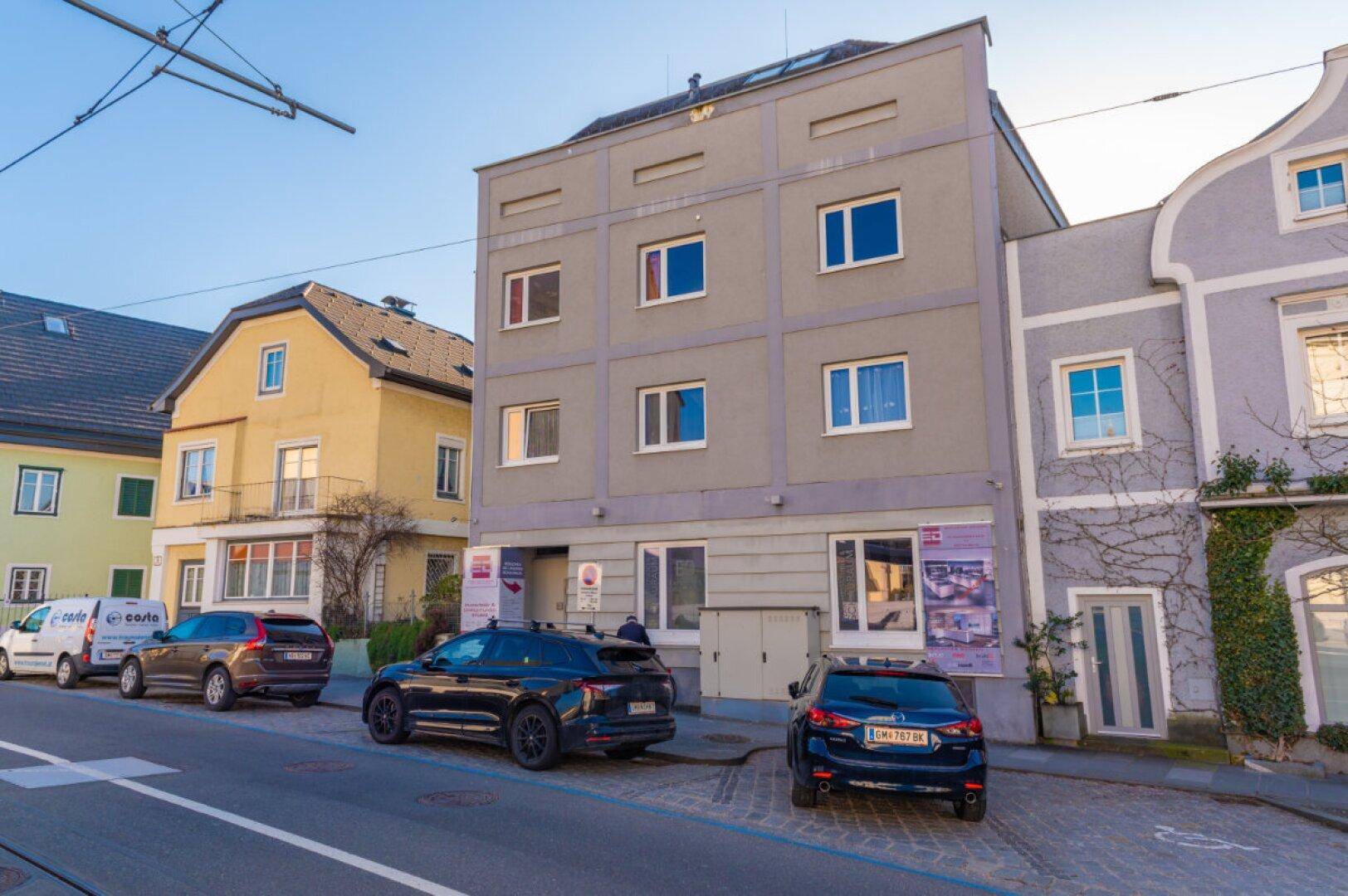 Stadthausfassade in Gmunden mit mehreren Fenstern und parkenden Autos auf der Straße.