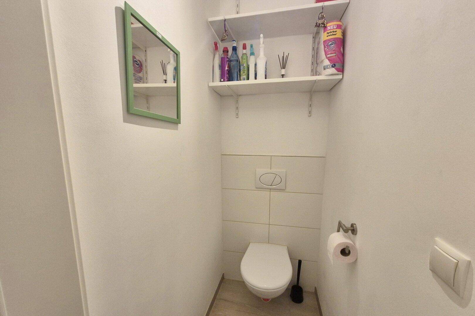 Kleine Gästetoilette mit Wand-WC und Regal für Utensilien, einfach gehalten.