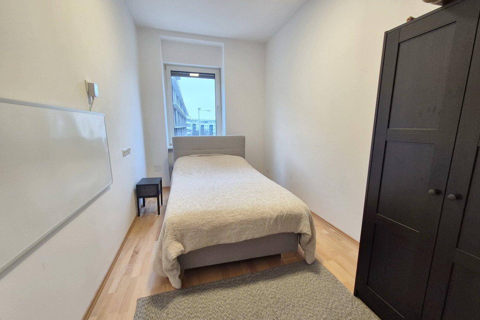Schlichtes Schlafzimmer mit Einzelbett, Kleiderschrank und Holzfußboden.