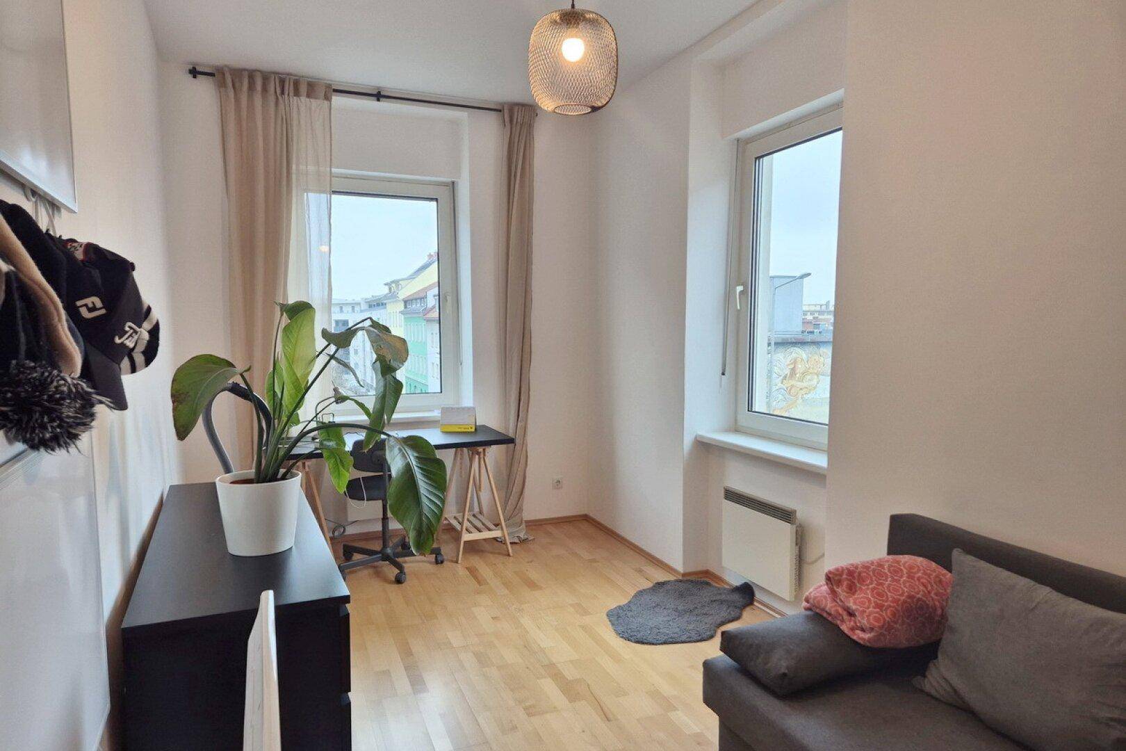 Heller Arbeitsbereich mit Schreibtisch am Fenster, Holzfußboden und einem Sofa.