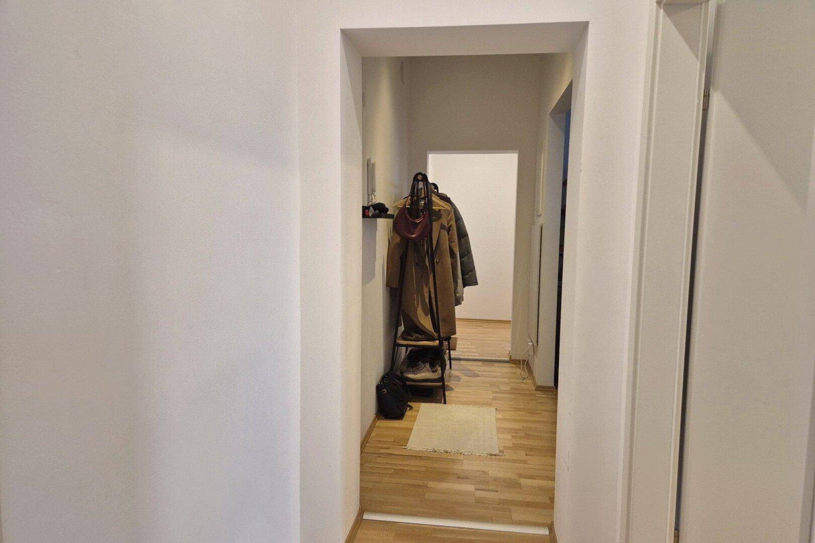 Schmaler Flur mit Holzfußboden und Garderobe, der zu weiteren Räumen führt.