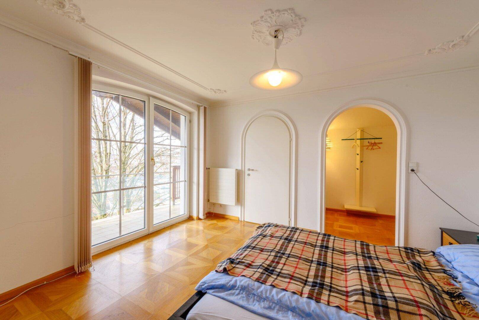 Helles Schlafzimmer mit Parkettboden, Stuckdecke und Zugang zum Balkon.