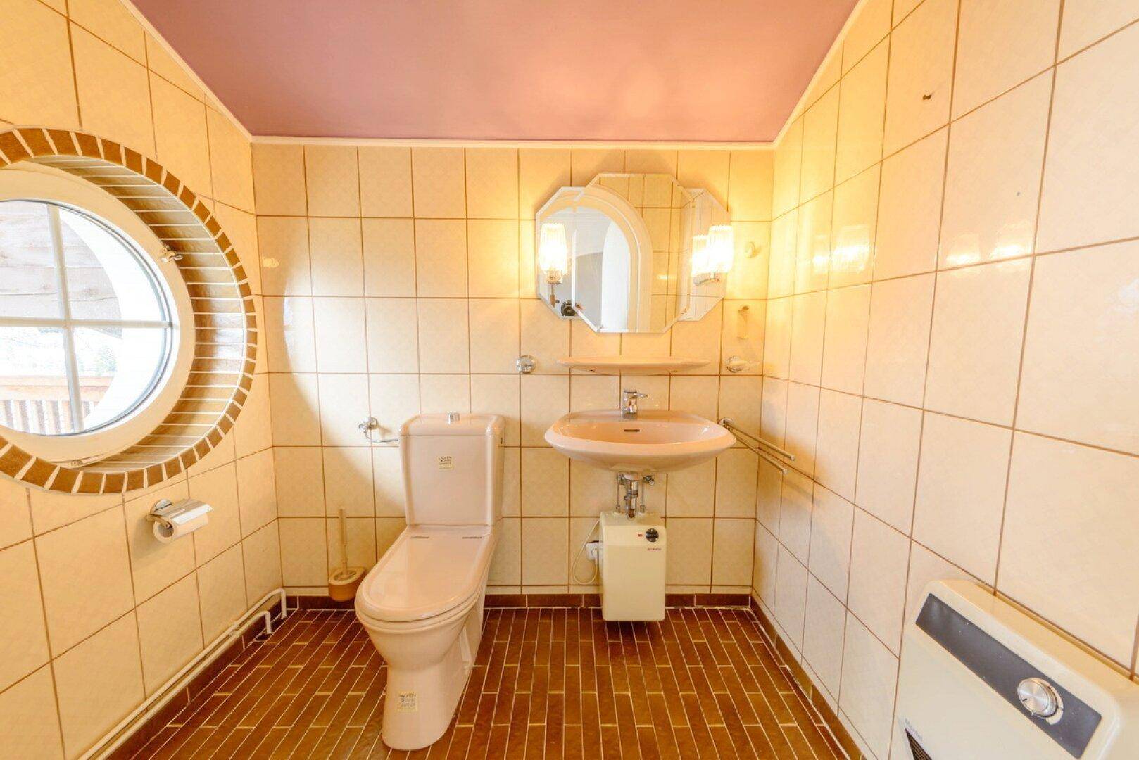 Gäste-WC mit beigefarbenen Fliesen, runden Fenstern und einfacher Ausstattung.