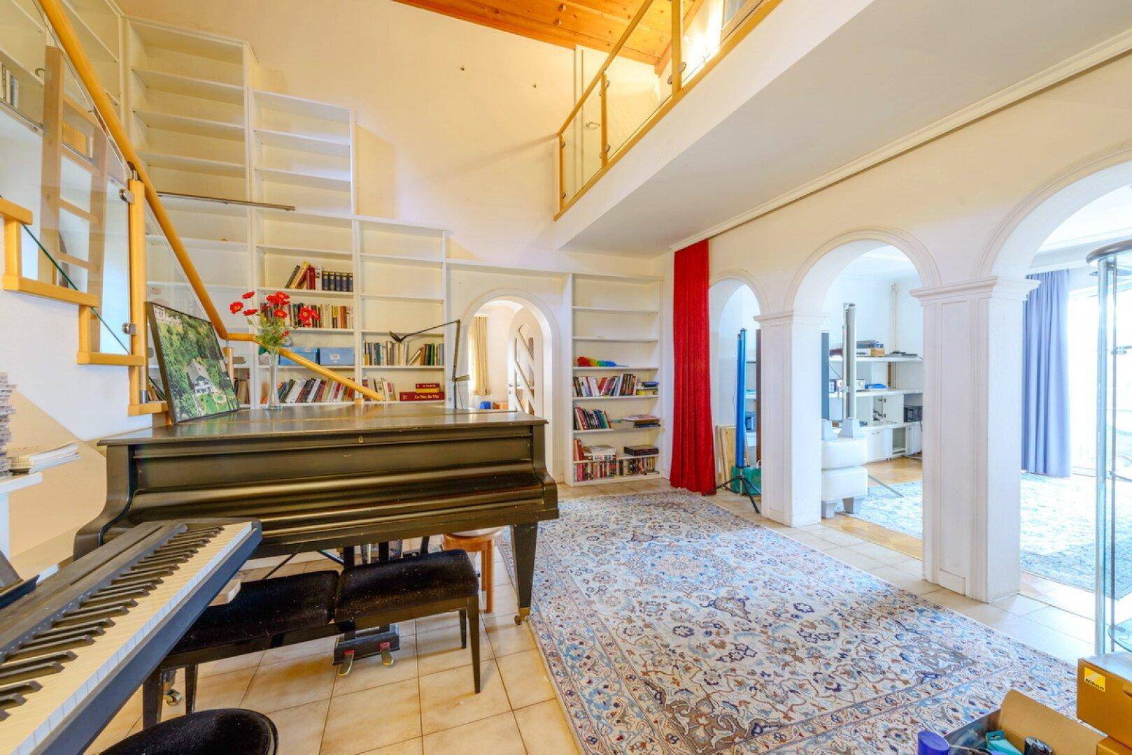 Geräumiger Wohnbereich mit Klavier, hohen Decken und integrierten Bücherregalen.