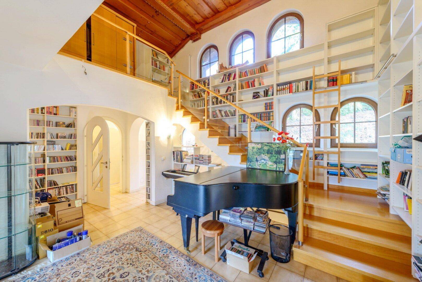 Lichtdurchfluteter Wohnraum mit Galerie, hohen Decken und umfangreichen Bücherregalen.