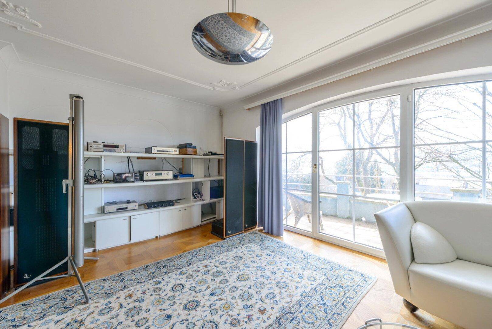 Heller Wohnraum mit Parkettboden, großem Fenster und Zugang zu einer Terrasse.