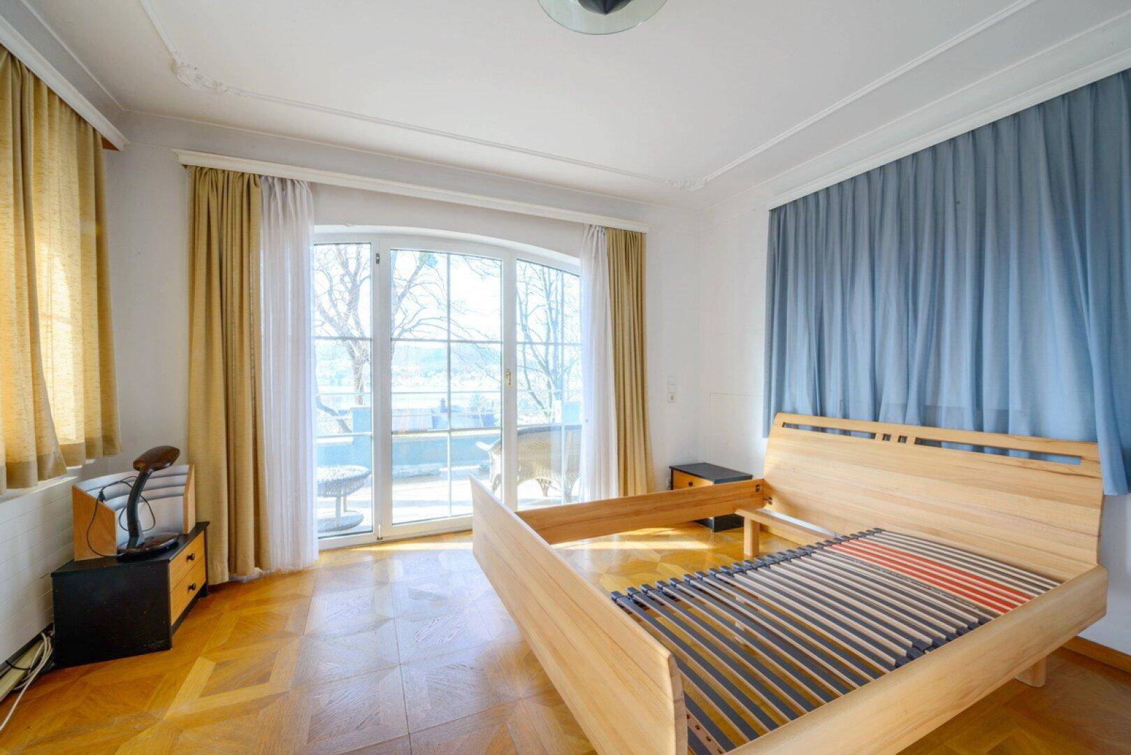 Geräumiges Schlafzimmer mit Holzbettrahmen, Parkettboden und Zugang zum Balkon.