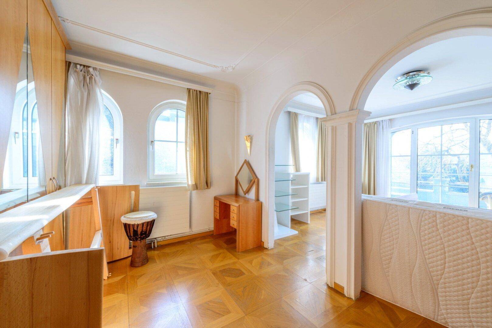 Lichtdurchflutetes Schlafzimmer mit Parkettboden, Rundbogenfenstern und Schminktisch.