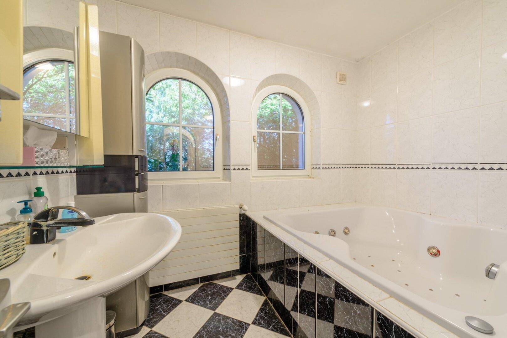 Badezimmer mit Whirlpool-Badewanne, Schachbrettmuster-Fliesen und Rundbogenfenstern.