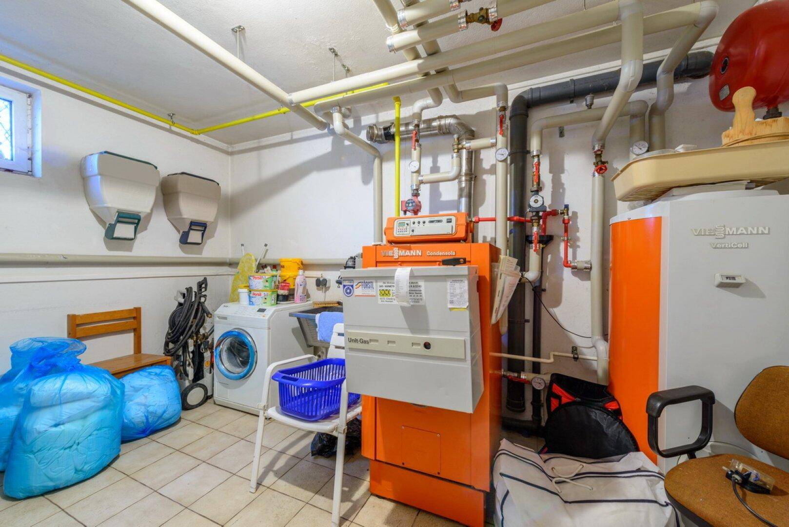 Technikraum mit Heizungsanlage, Waschmaschine und sichtbaren Installationen.