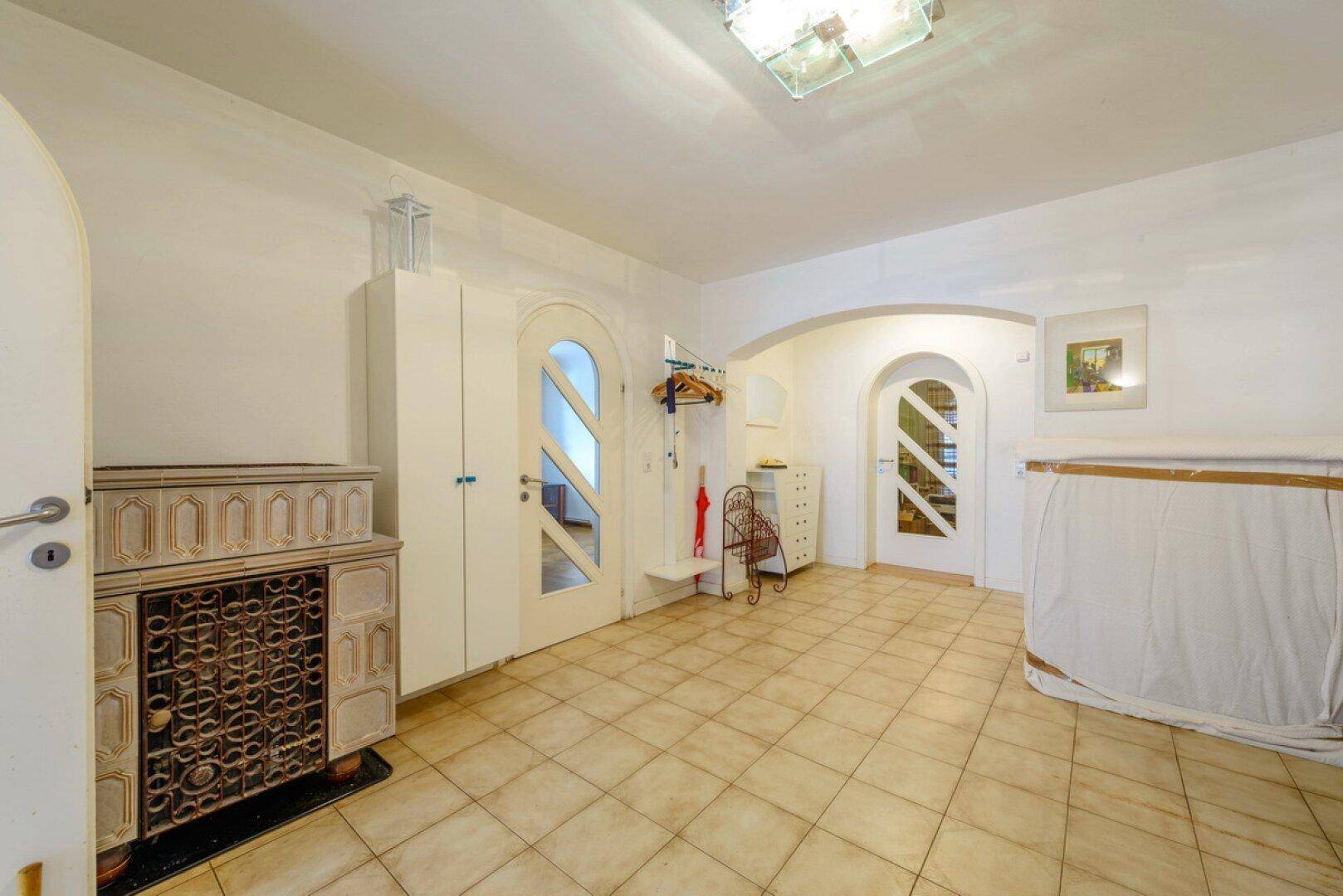 Geräumiger Eingangsbereich mit Fliesenboden, Kachelofen und Garderobe.