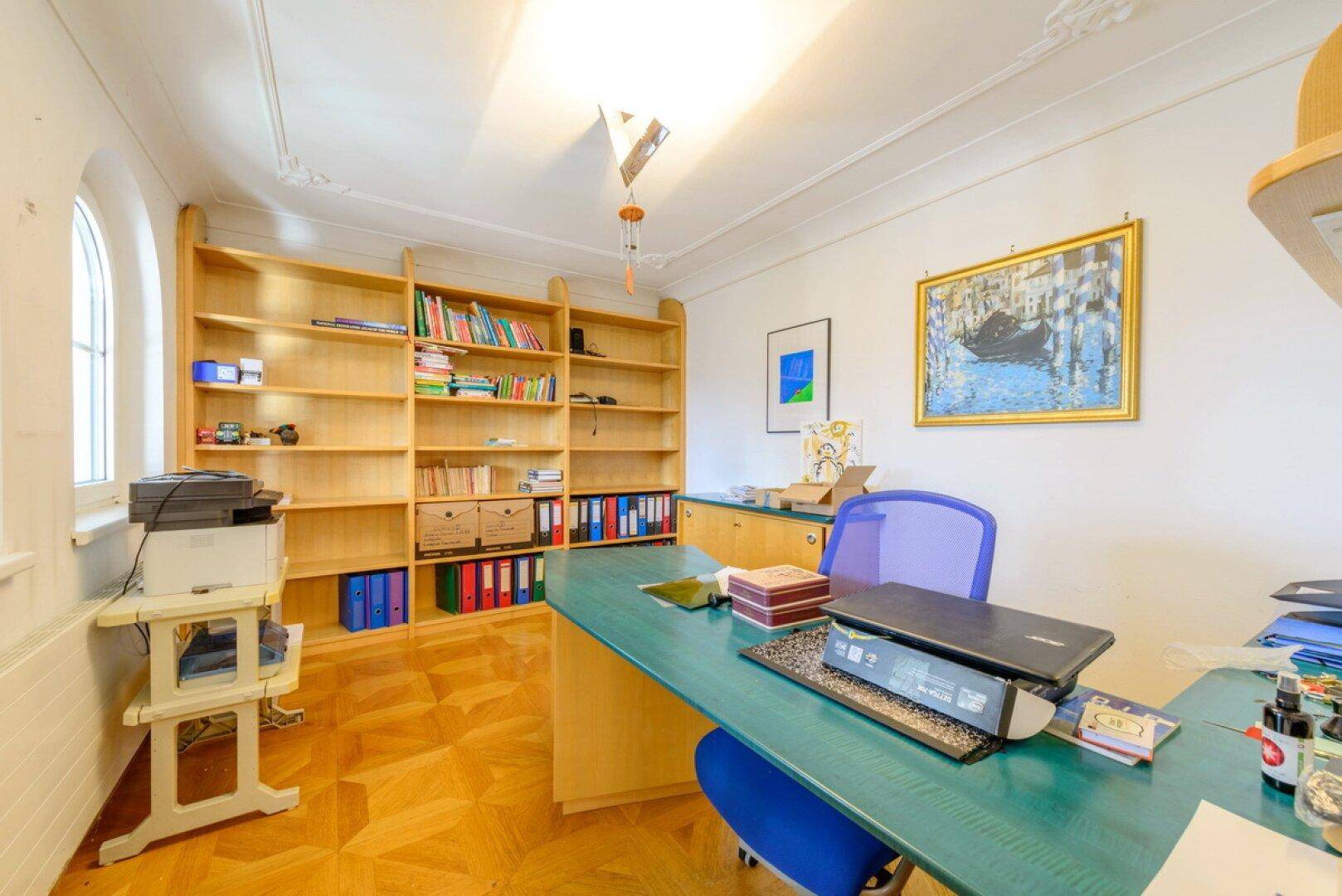 Funktionales Büro mit Parkettboden, großem Schreibtisch und Bücherregalen.