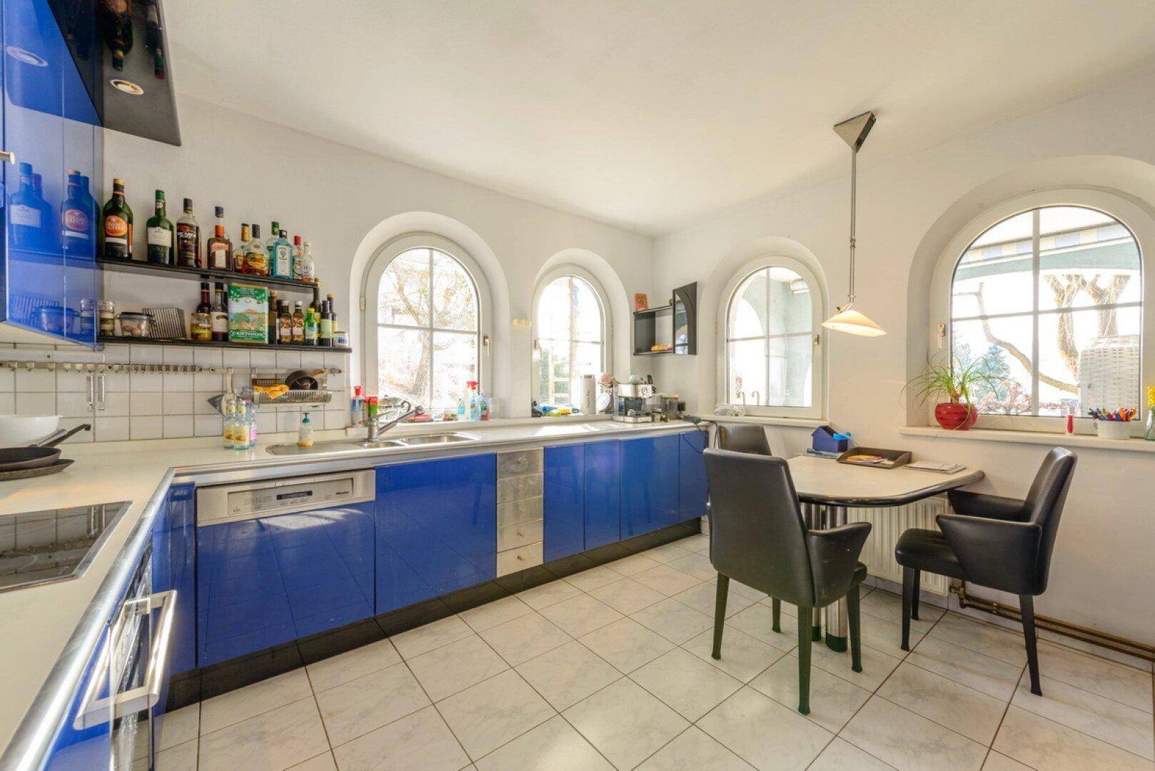 Moderne Küche mit blauen Schränken, Fliesenboden und Rundbogenfenstern.