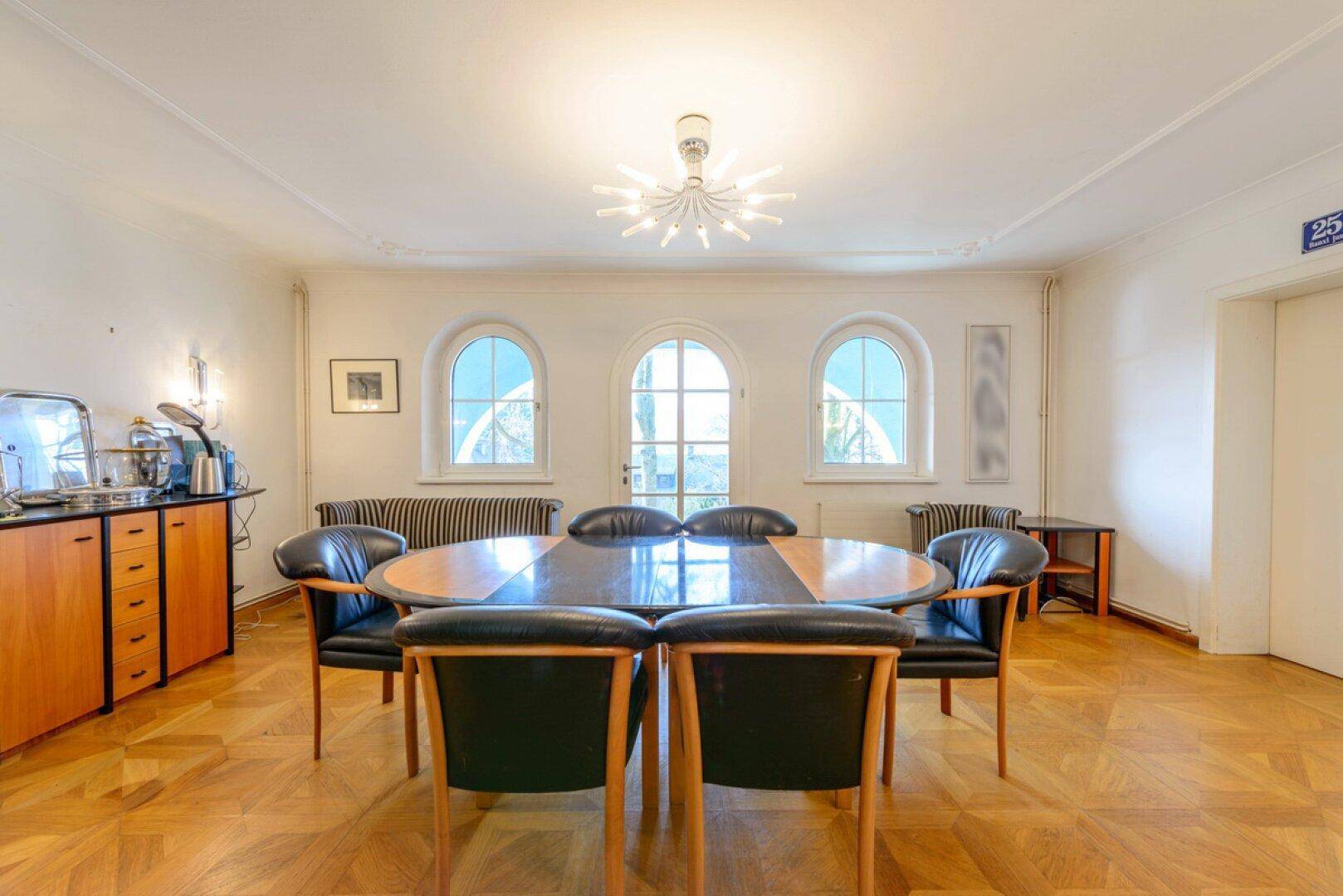 Eleganter Essbereich mit Parkettboden, Rundbogenfenstern und modernem Kronleuchter.