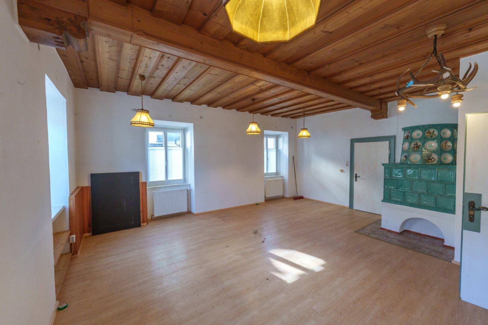 Geräumiger Wohnbereich mit Holzbalkendecke, Parkettboden und traditionellem Kachelofen.