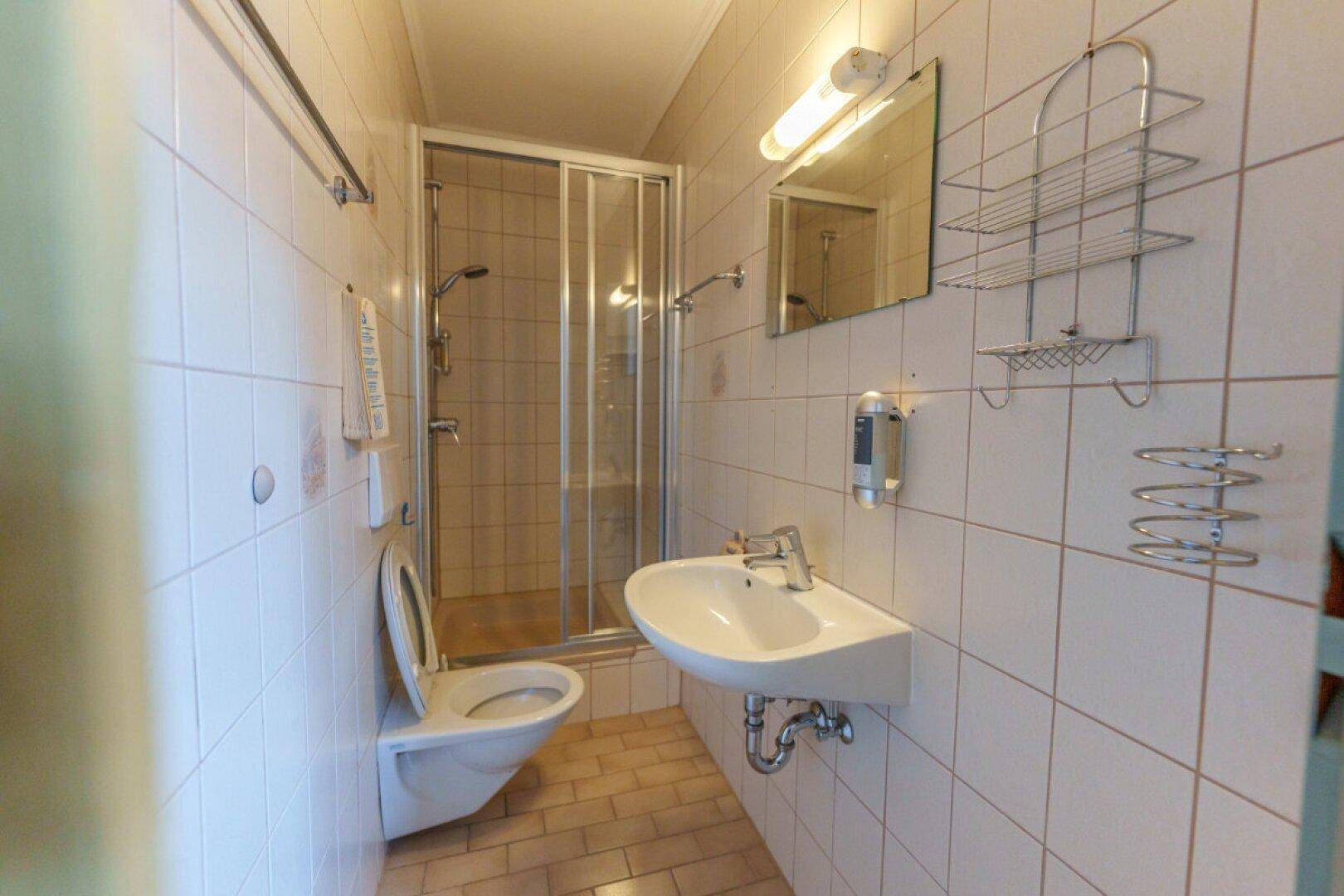 Funktionales Badezimmer mit Dusche, WC und Waschbecken, gefliest in hellen Tönen.