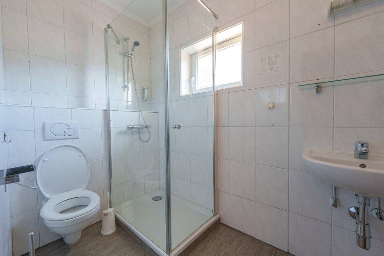 Modernes Badezimmer mit Duschkabine, WC, Waschbecken und Fenster.