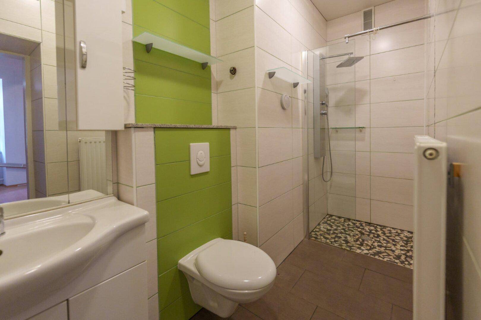Modernisiertes Badezimmer mit begehbarer Dusche, WC und grün akzentuierter Wand.