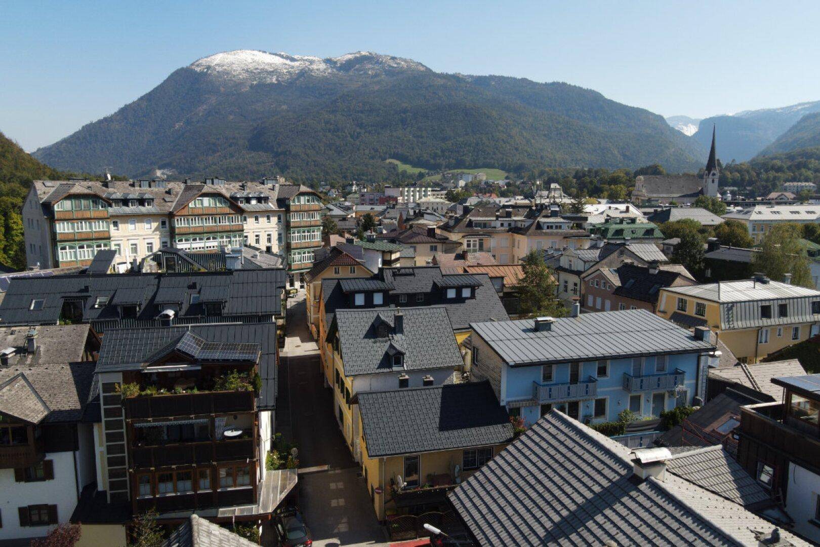 Luftaufnahme der Stadt mit vielen Dächern und einem großen Berg im Hintergrund.