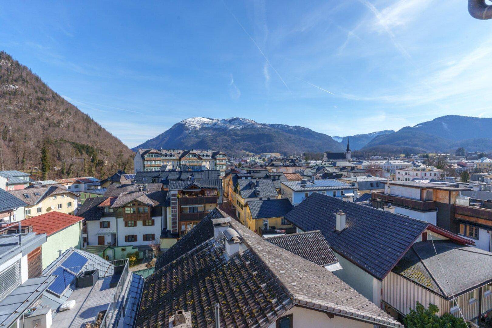 Weitläufiger Blick über die Dächer der Stadt mit Bergen und Himmel im Hintergrund.