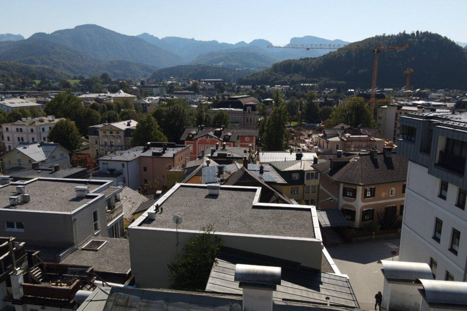 Dachlandschaft der Stadt mit grünen Hügeln und einem Kran am Horizont.