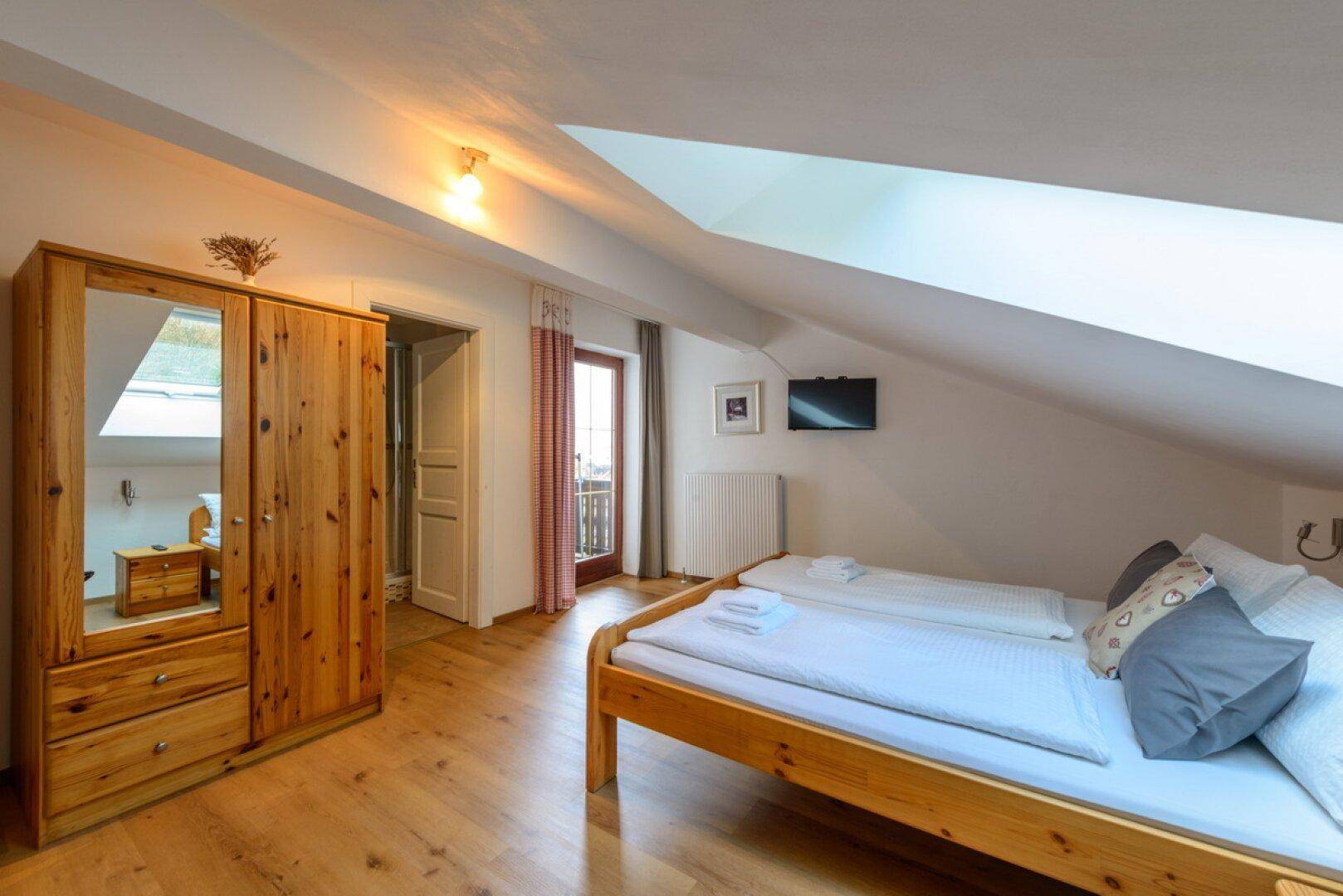Gemütliches Schlafzimmer im Dachgeschoss mit Holzboden, Dachschräge und Balkonzugang.