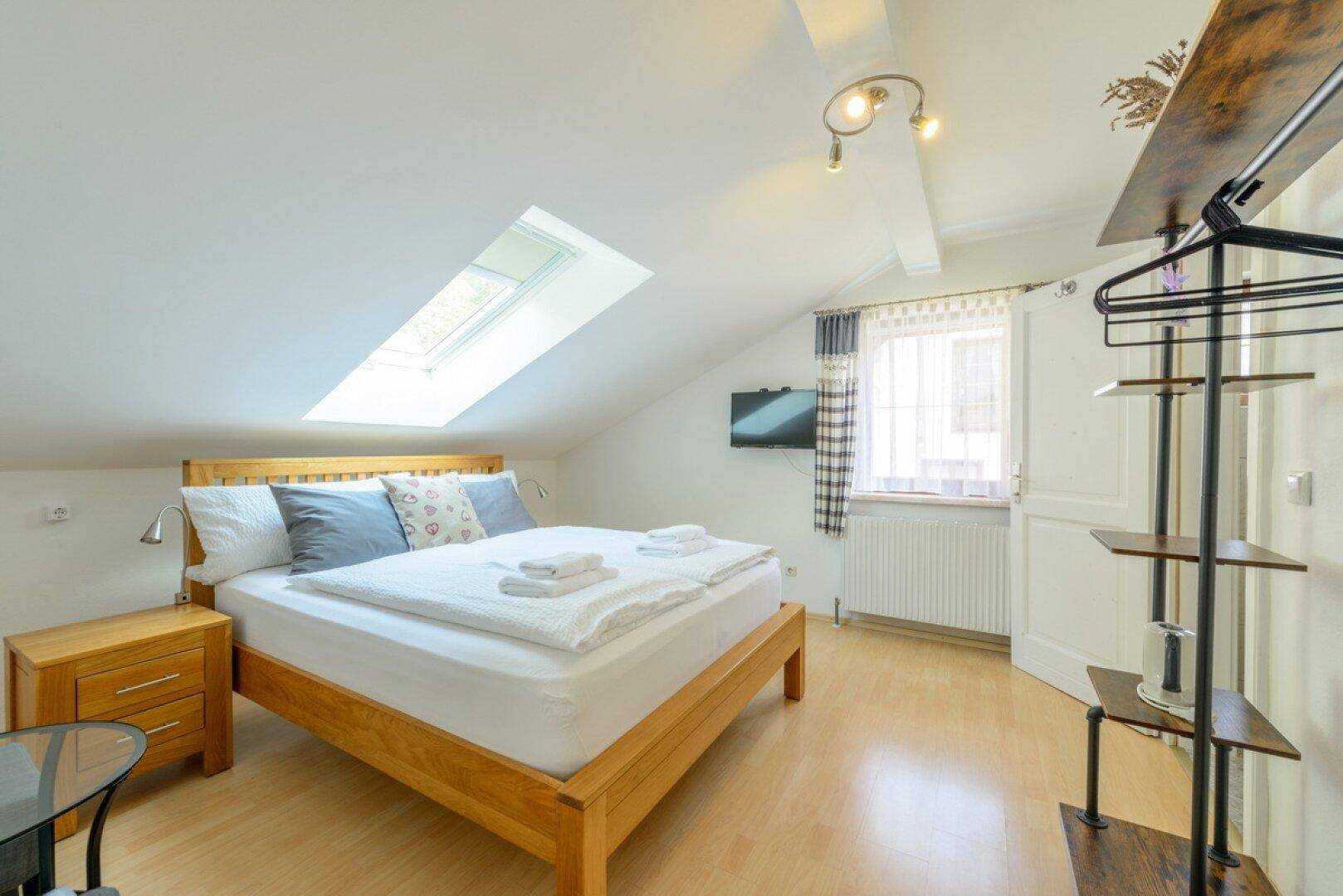 Lichtdurchflutetes Schlafzimmer im Dachgeschoss mit Holzbett und Dachfenster.