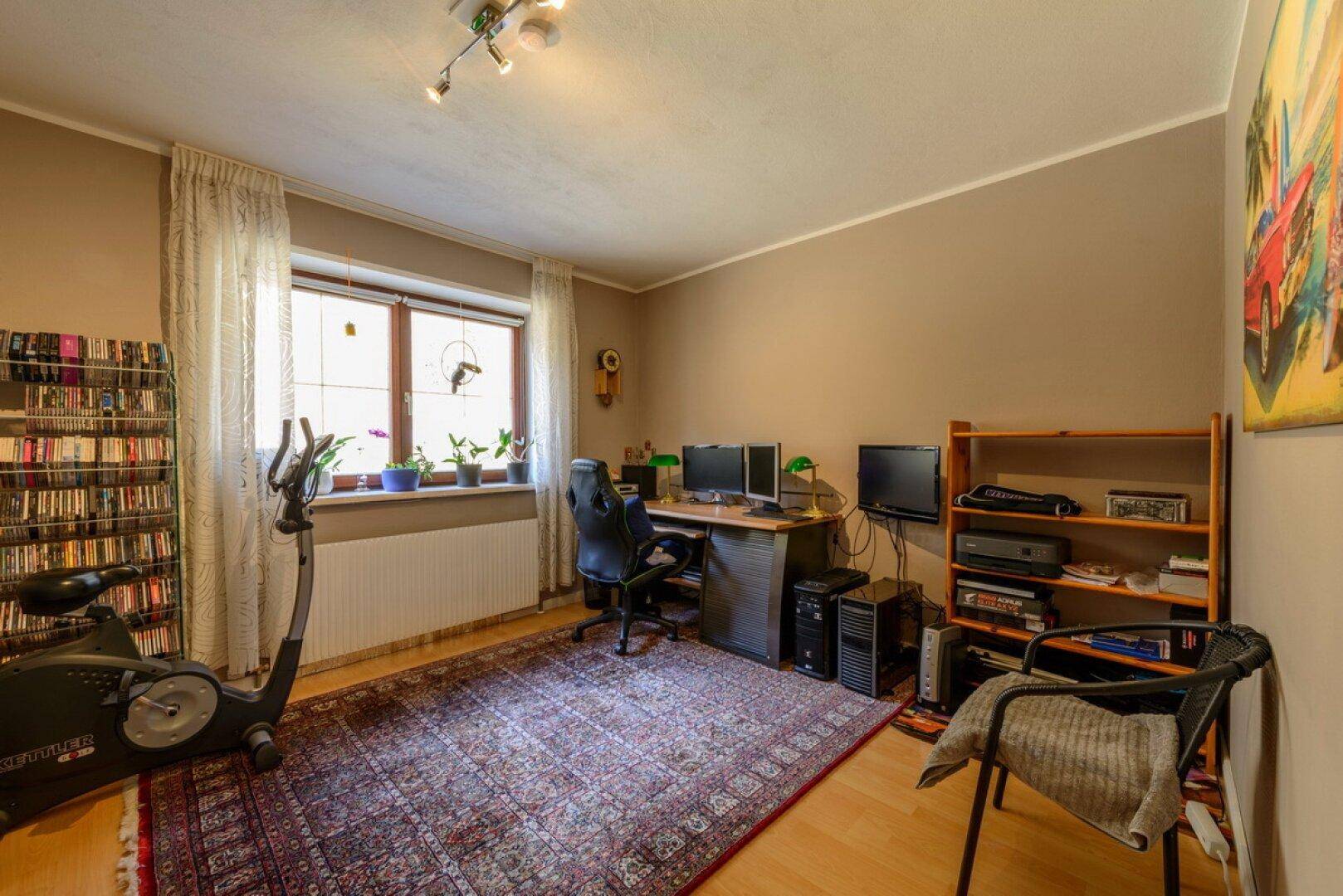 Geräumiges Arbeitszimmer mit Schreibtisch, Bücherregalen und Trainingsgerät.