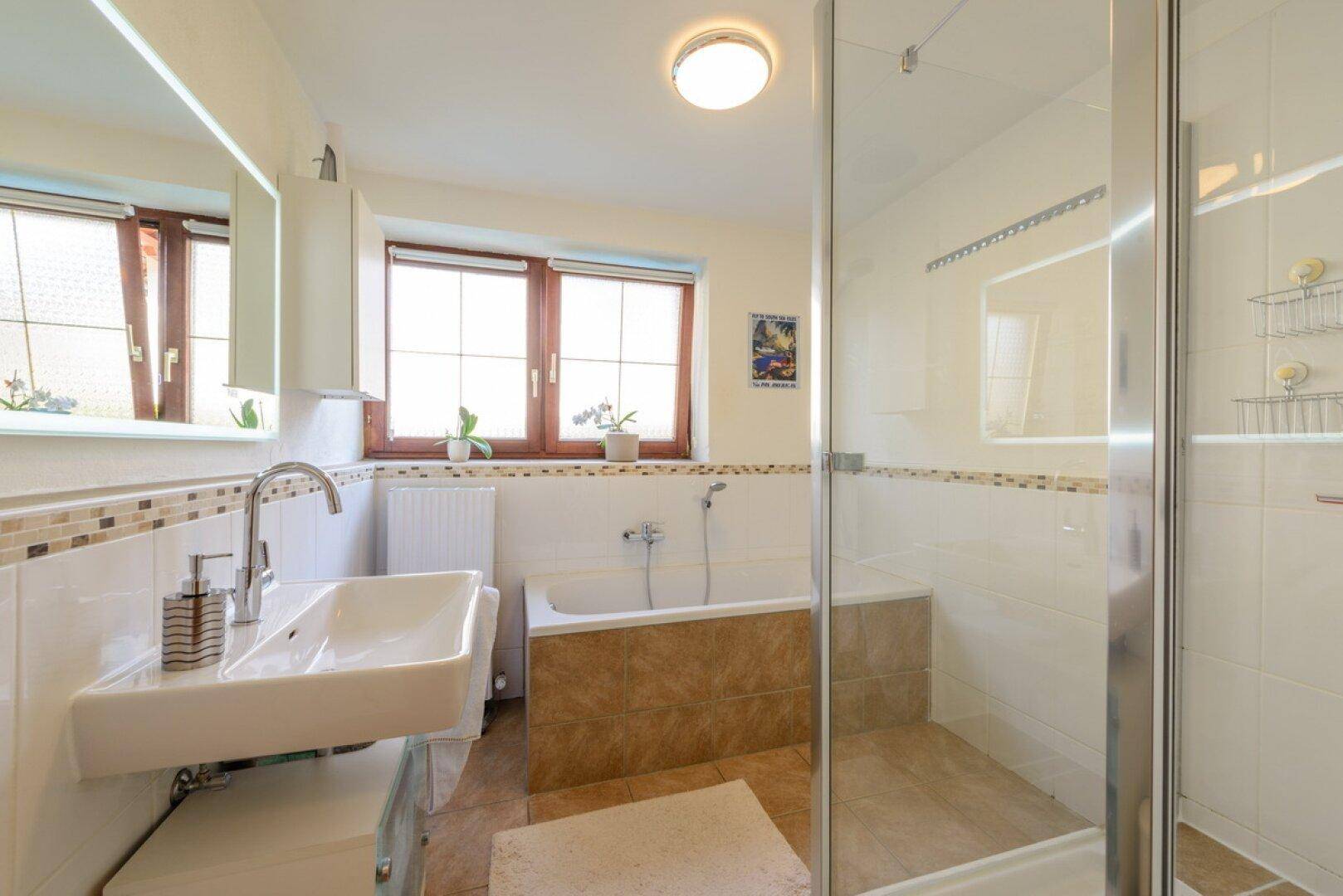 Modernes Badezimmer mit Badewanne, Duschkabine und Fenster für Tageslicht.