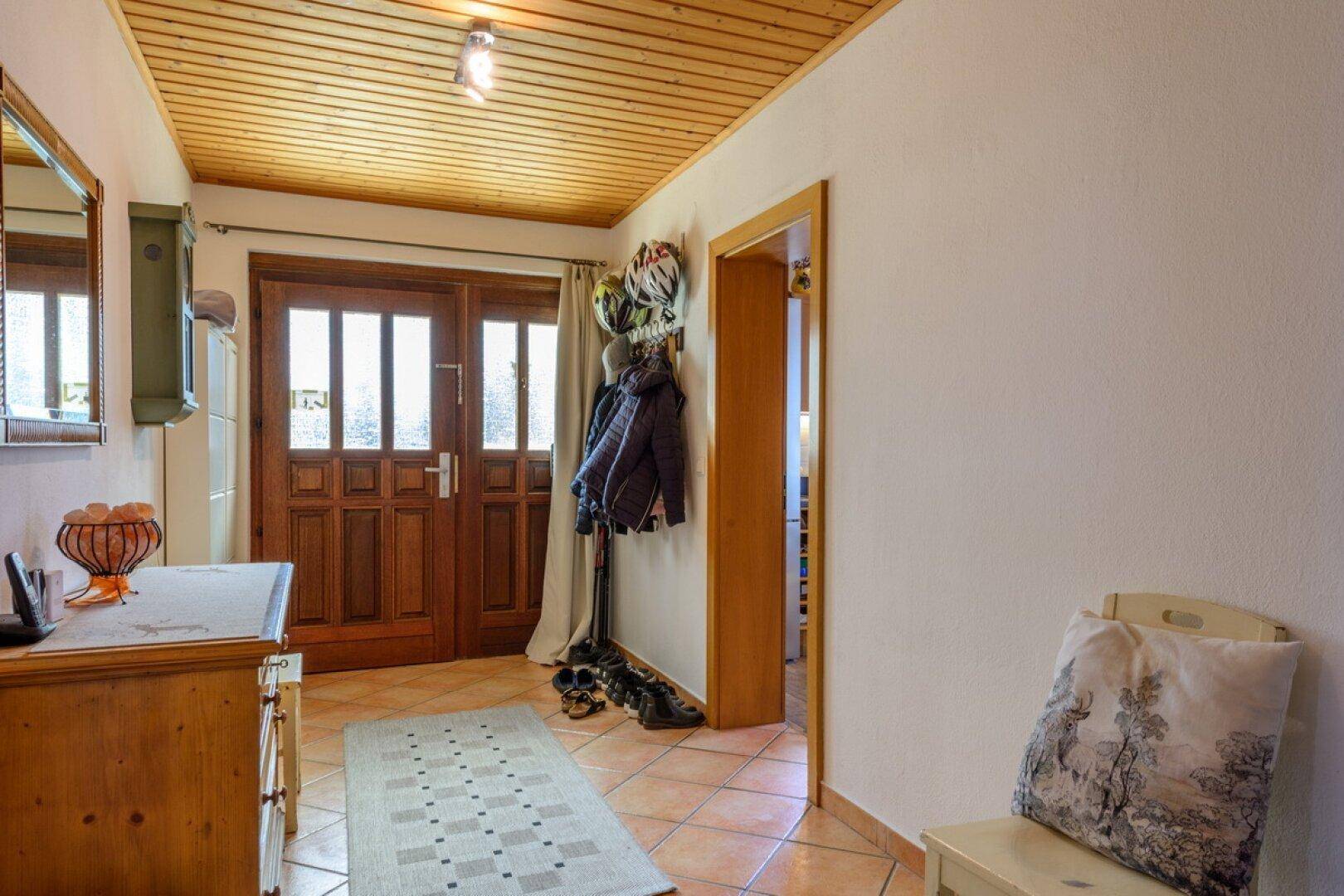 Einladender Eingangsbereich mit Terrakottafliesen, Holzdecke und Garderobe.