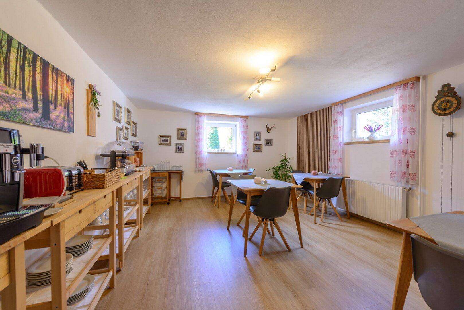 Heller Frühstücksraum mit mehreren Tischen, Holzmöbeln und Laminatboden.