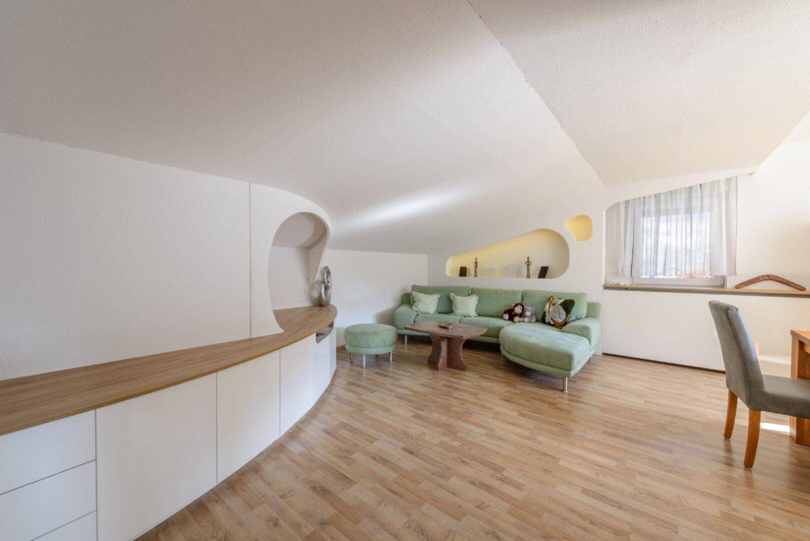 Heller Wohnbereich mit Sofa, Einbauschränken und Holzboden unter einer Dachschräge.