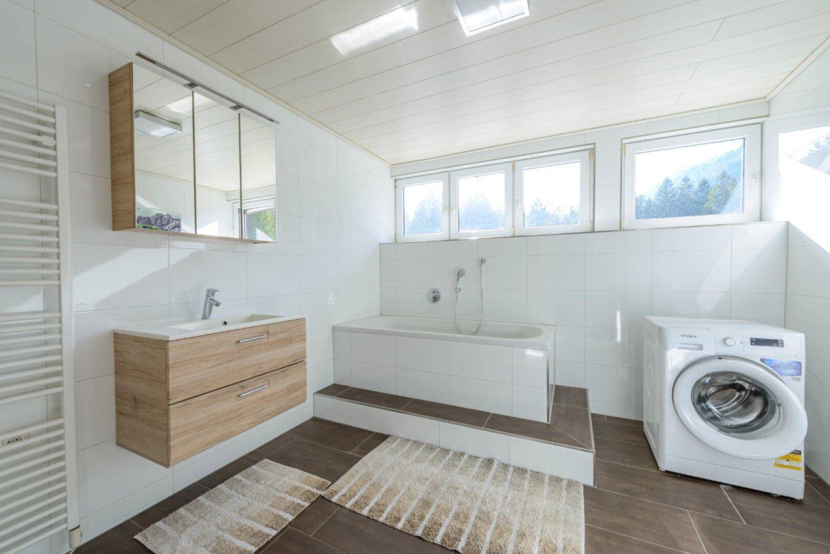 Helles Badezimmer mit Badewanne, Waschmaschine und Fenster mit Bergblick.