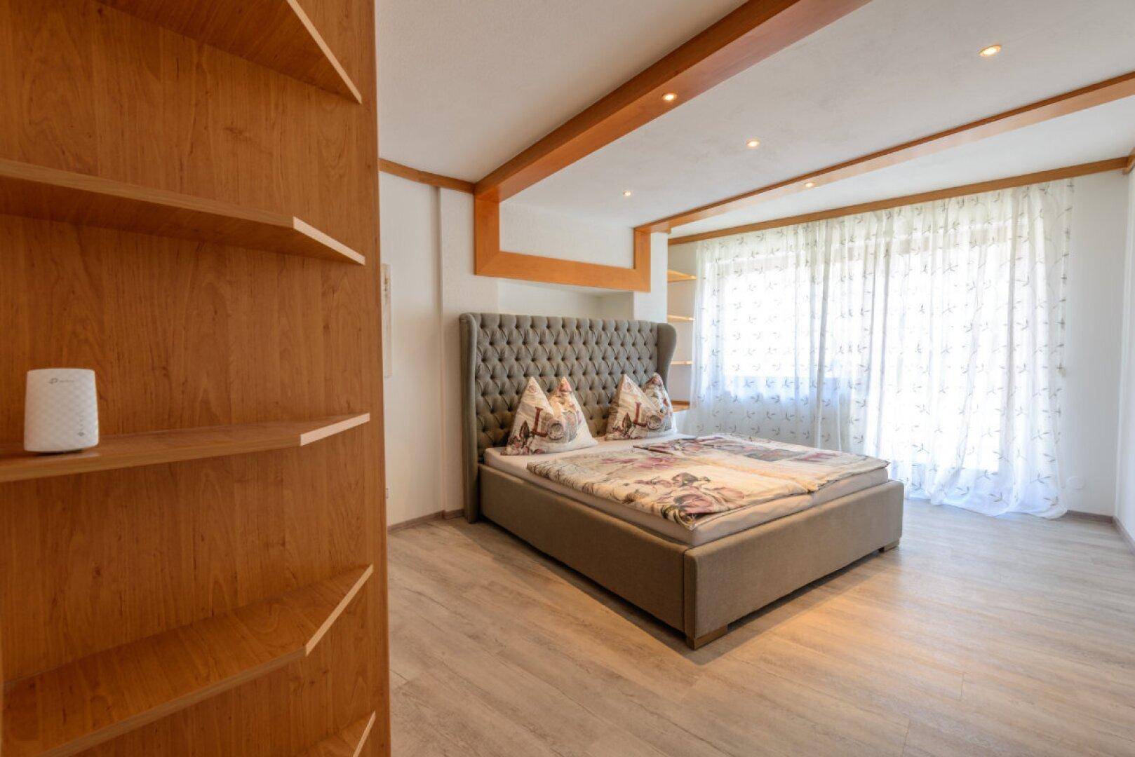 Geräumiges Schlafzimmer mit Doppelbett, Holzbalken und Einbauregalen sowie hellem Boden.