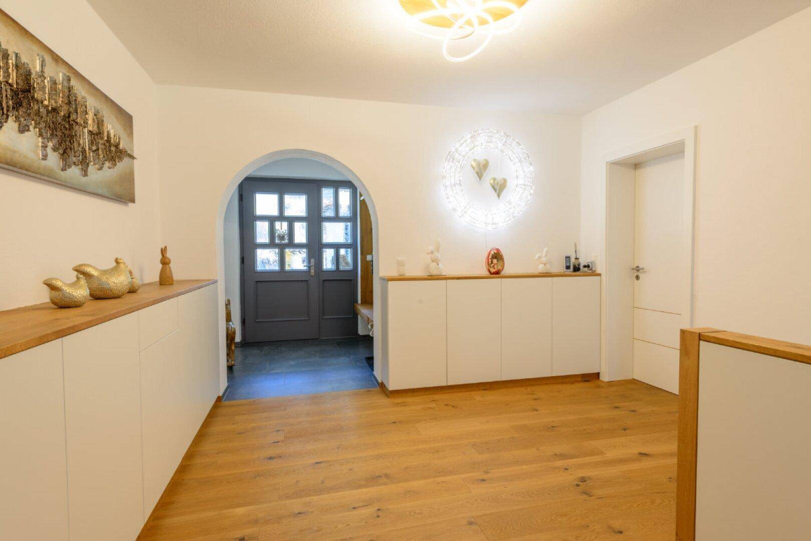 Heller Eingangsbereich mit Holzparkettboden, modernen Einbauschränken und dekorativer Beleuchtung.